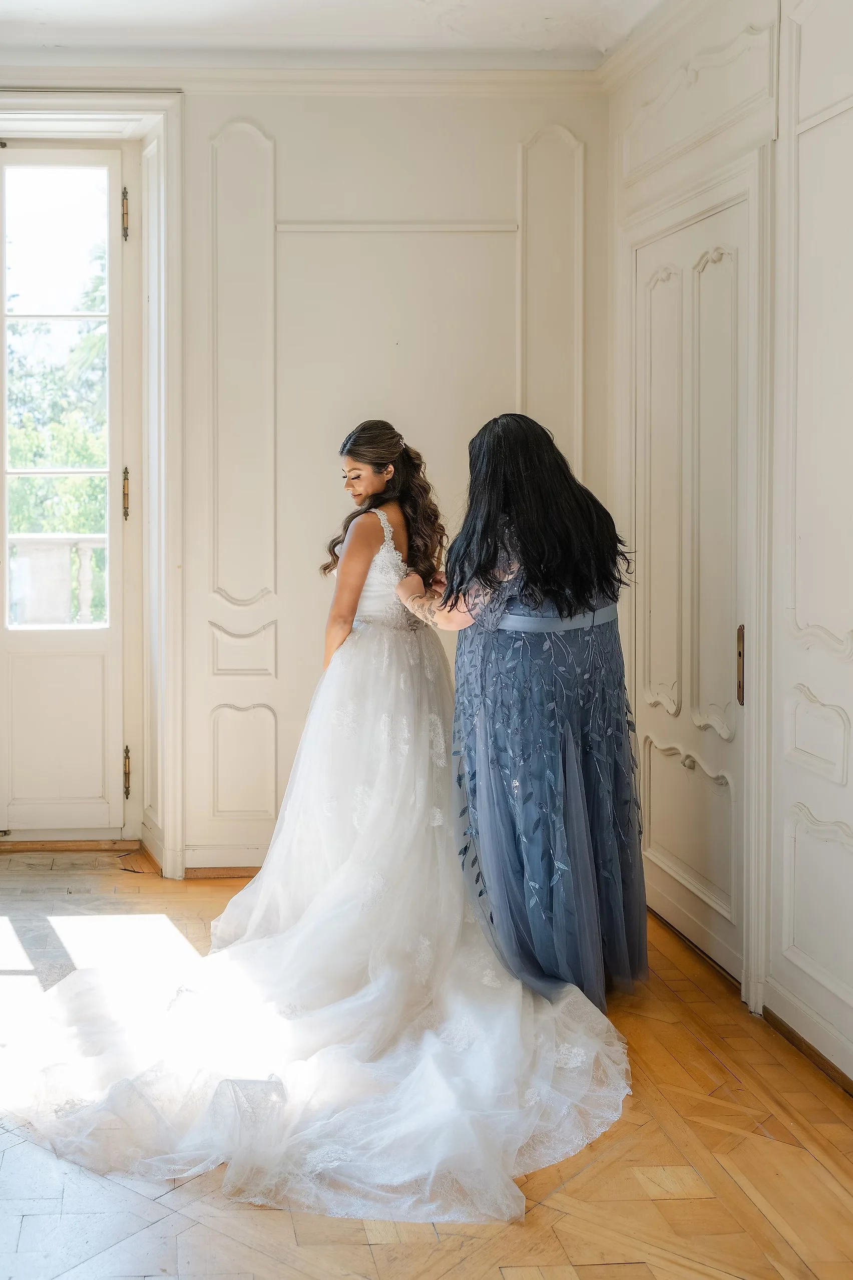 Ashley Rodriguez-Vargas being helped into her wedding gown by a loved one in a bright room at Villa Emden, Brissago Island.