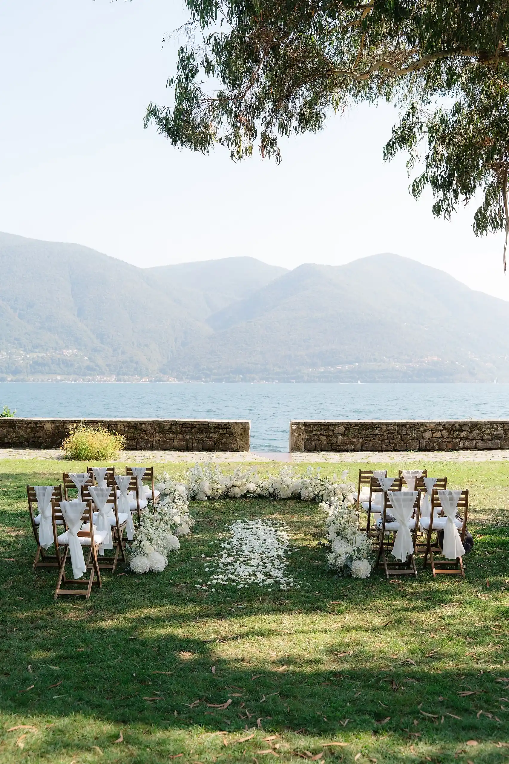 Outdoor wedding ceremony setup at Villa Emden on Brissago Island, Switzerland, with white floral arch and lake views.