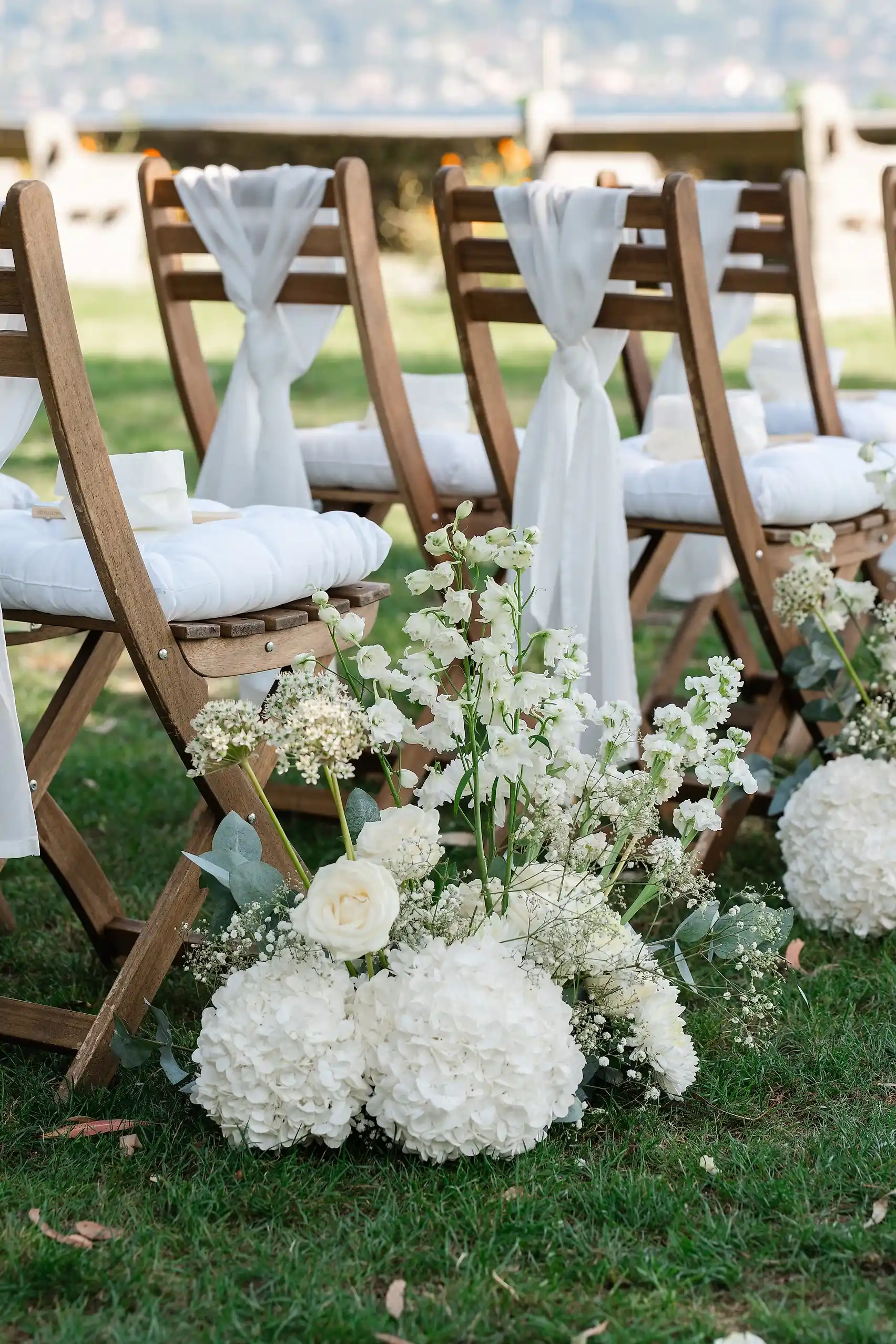White hydrangea and rose floral arrangements line the aisle at Ashley Rodriguez-Vargas and Dionne Vargas's outdoor ceremony at Villa Emden on Brissago Island, Switzerland.