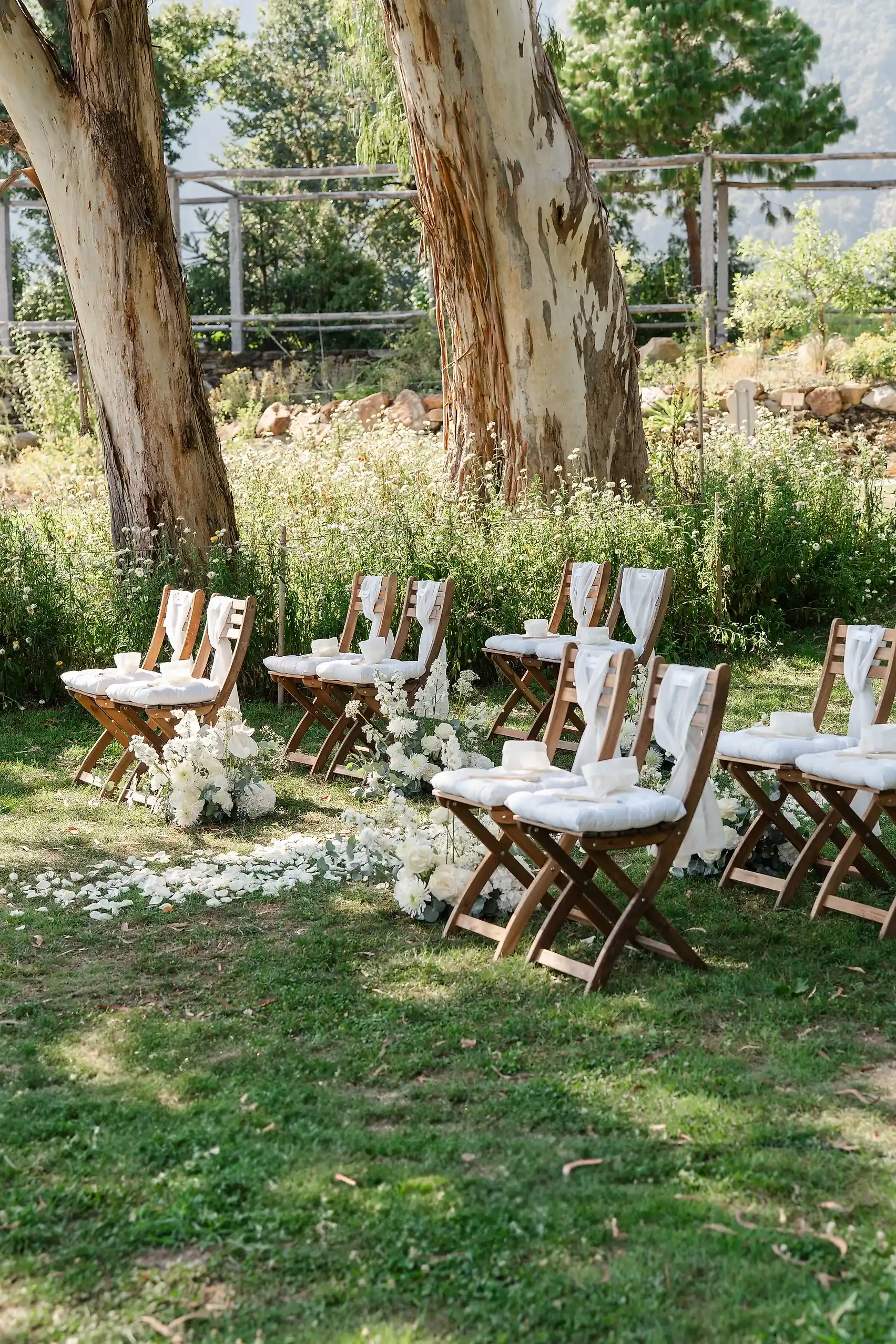 Wooden folding chairs with white cushions and floral aisle decor set for an outdoor wedding ceremony at Villa Emden, Brissago Island.
