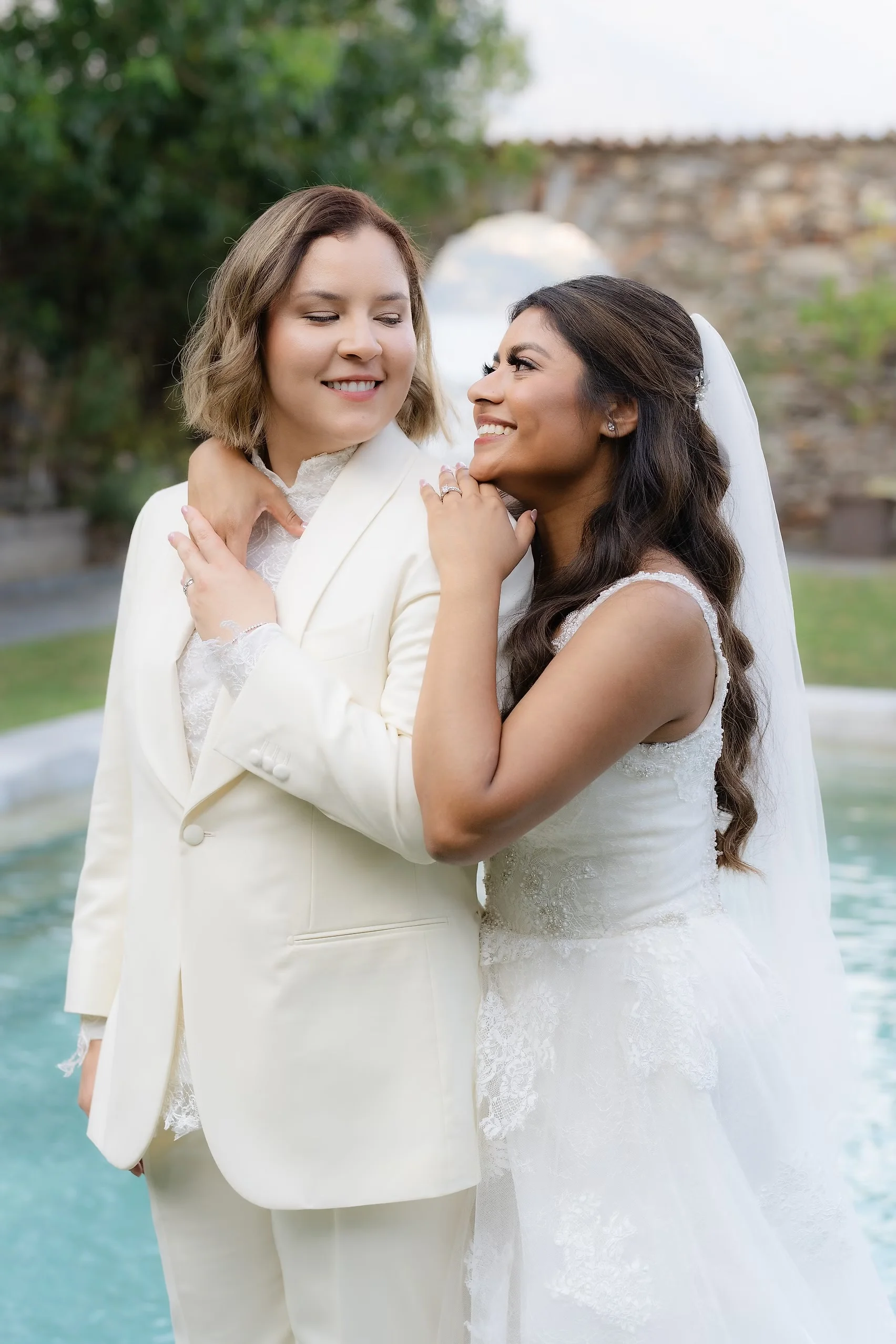 Brides Ashley Rodriguez-Vargas and Dionne Vargas embrace and smile by a fountain at Villa Emden on Brissago Island, Switzerland.
