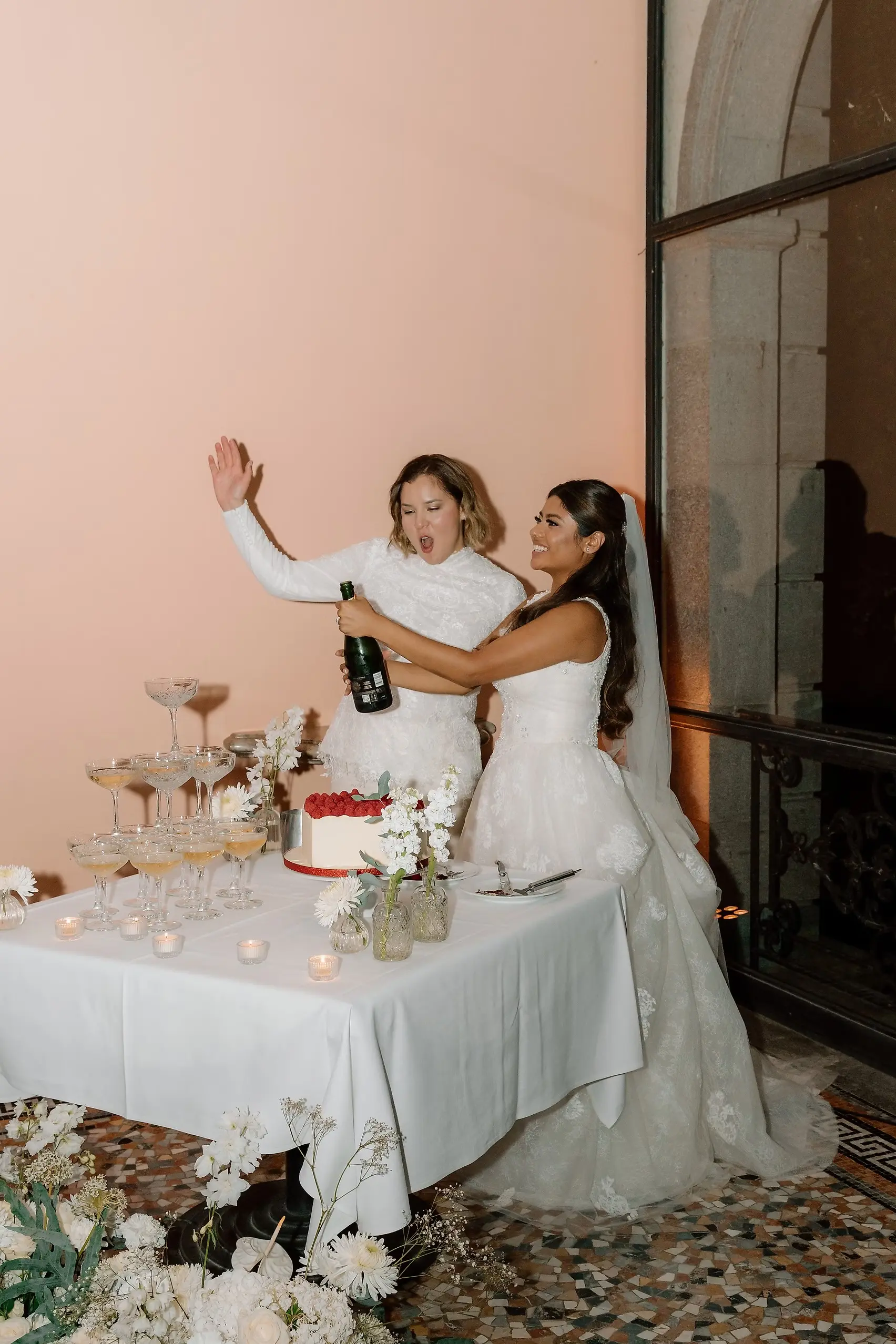 Ashley and Dionne pop champagne beside their wedding cake and tower of coupes at Villa Emden on Brissago Island.