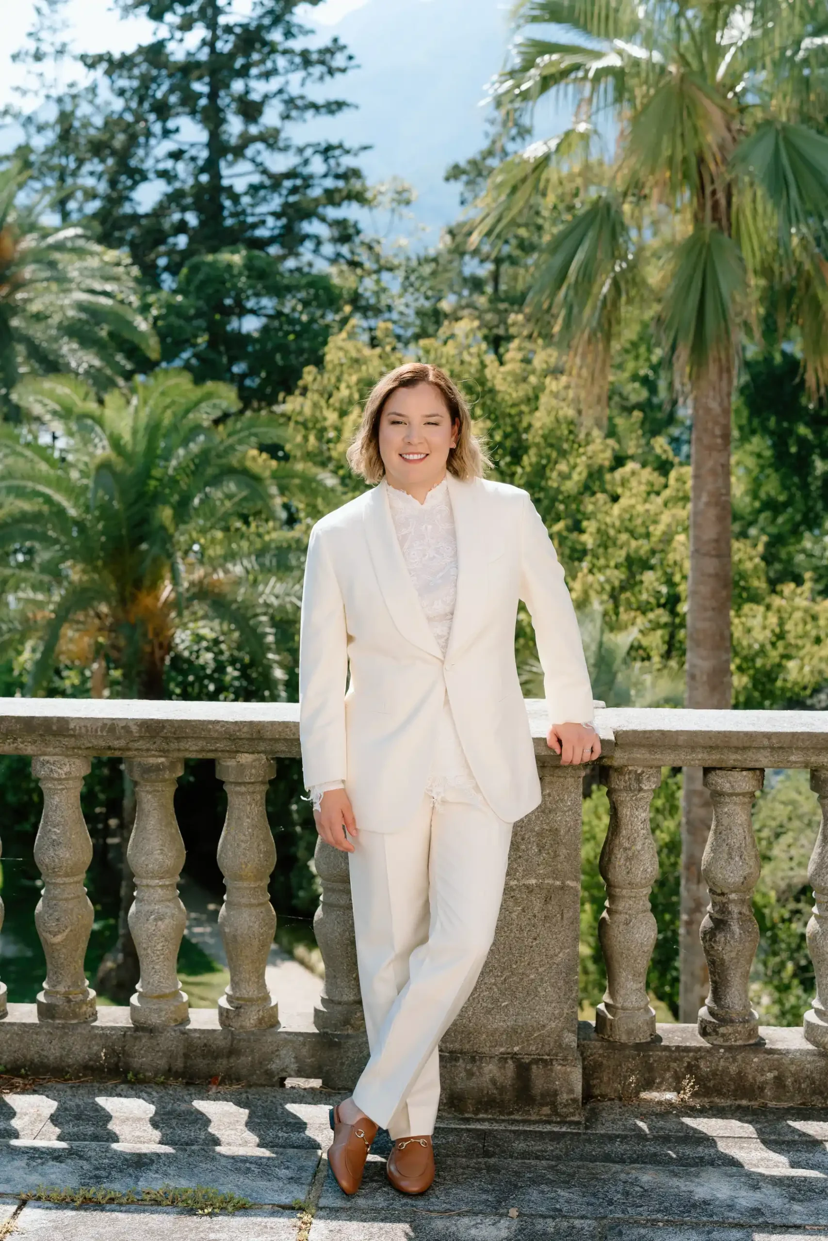 Ashley Rodriguez-Vargas poses in a white suit on the stone terrace at Villa Emden, Brissago Island, Switzerland.