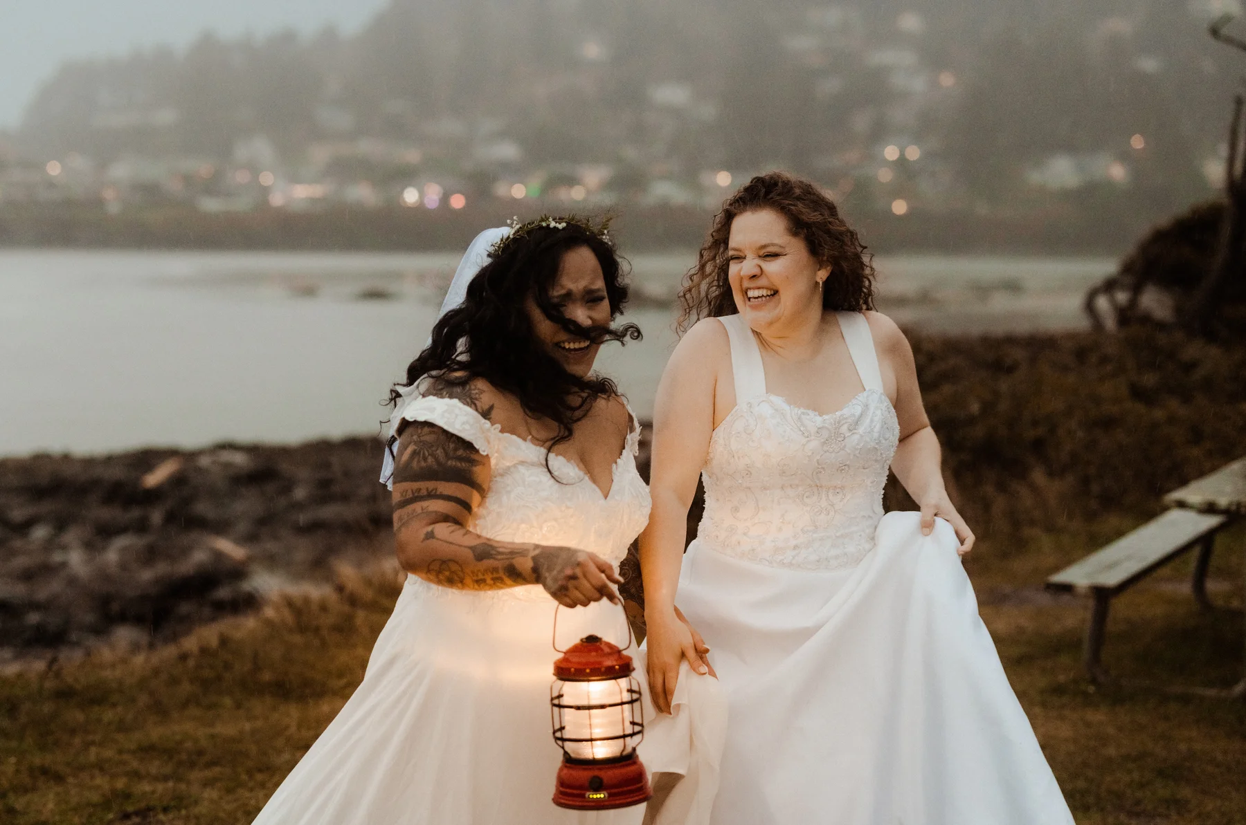 Brides Rachel and Jamie Snow laugh together holding a lantern at dusk near the coast at Yachats Inn, Oregon.