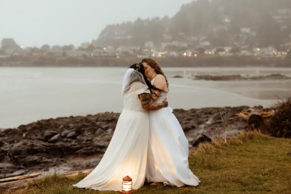 Brides Rachel and Jamie Snow share their first kiss in white gowns by the Oregon coast at Yachats Inn.