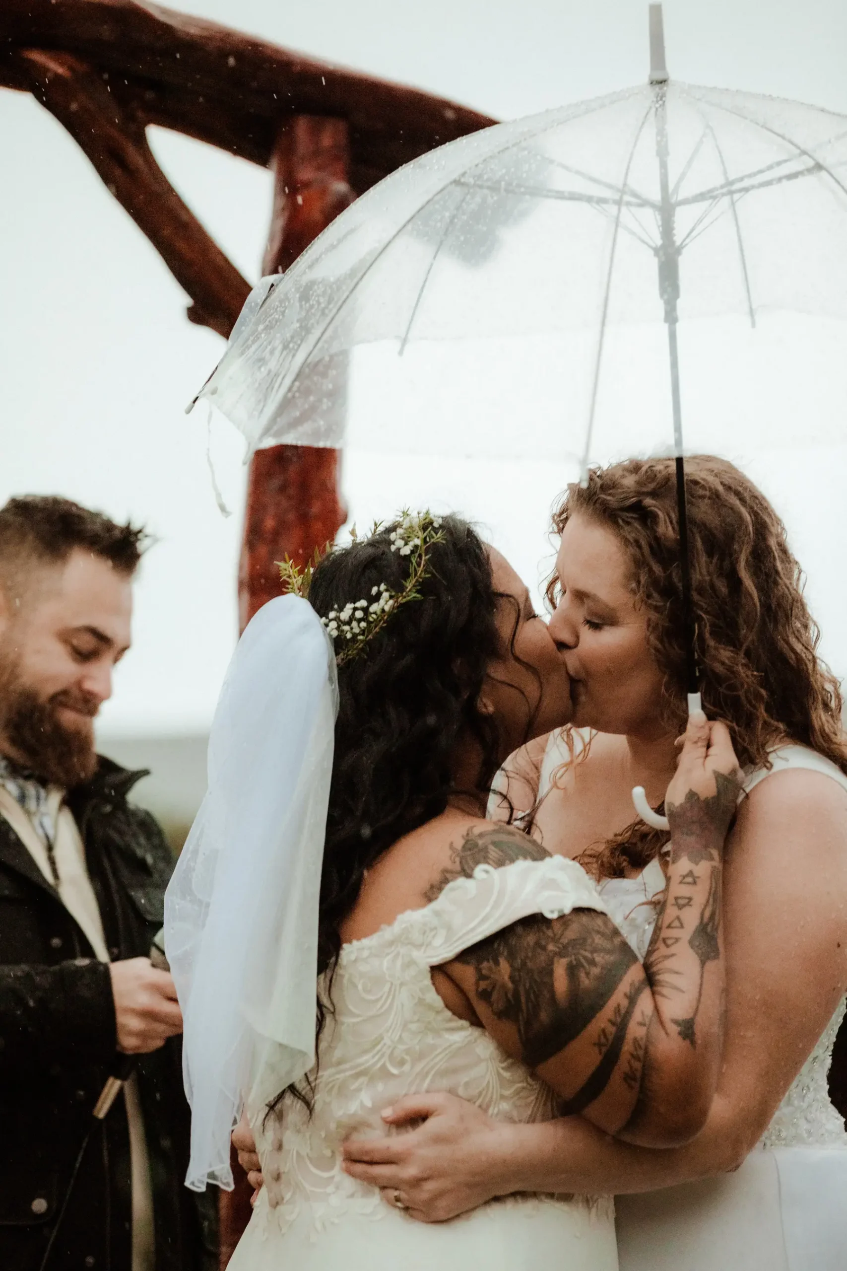 Brides Rachel Snow and Jamie Snow share their first kiss under a clear umbrella in the rain at Yachats Inn in Oregon.