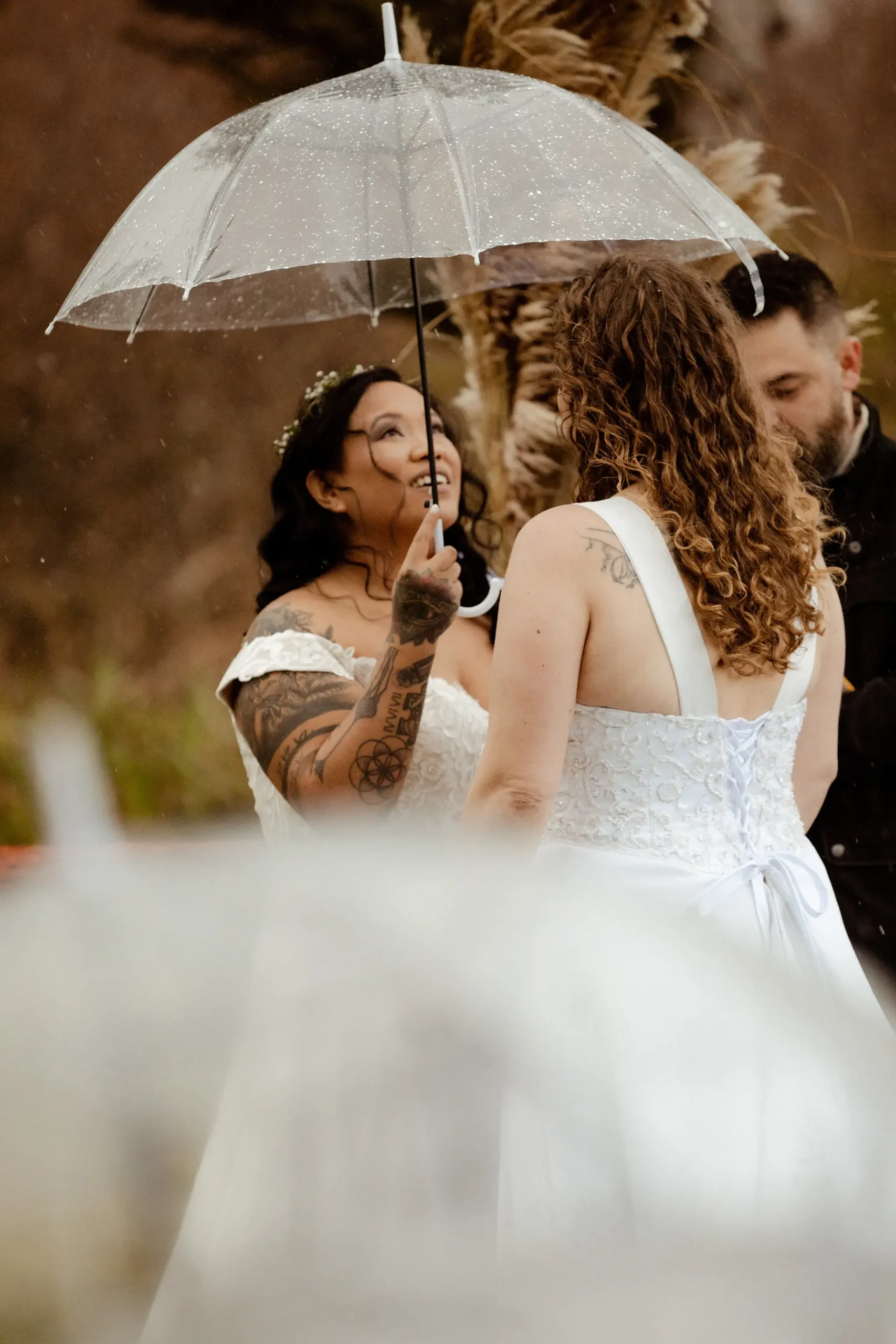 Brides Rachel and Jamie Snow share a joyful moment under a clear umbrella in the rain at Yachats Inn, Oregon.