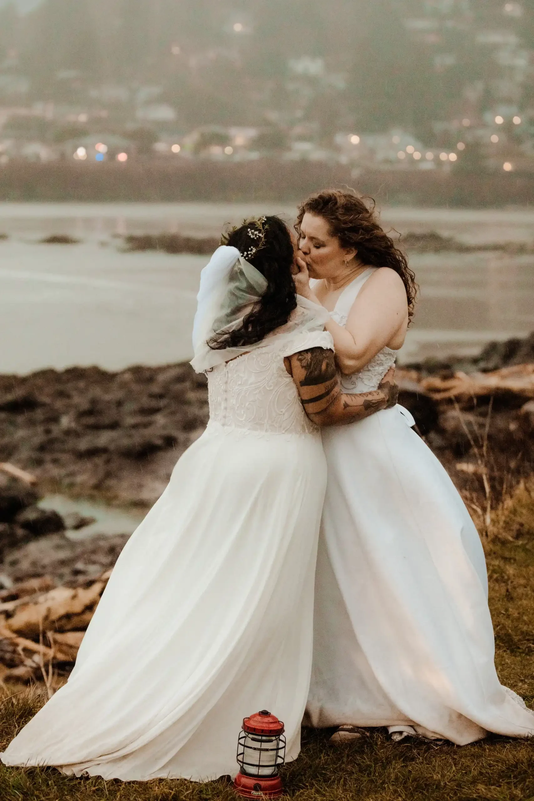 Brides Rachel and Jamie Snow share their first kiss in white gowns on a coastal cliff at Yachats Inn, Oregon.