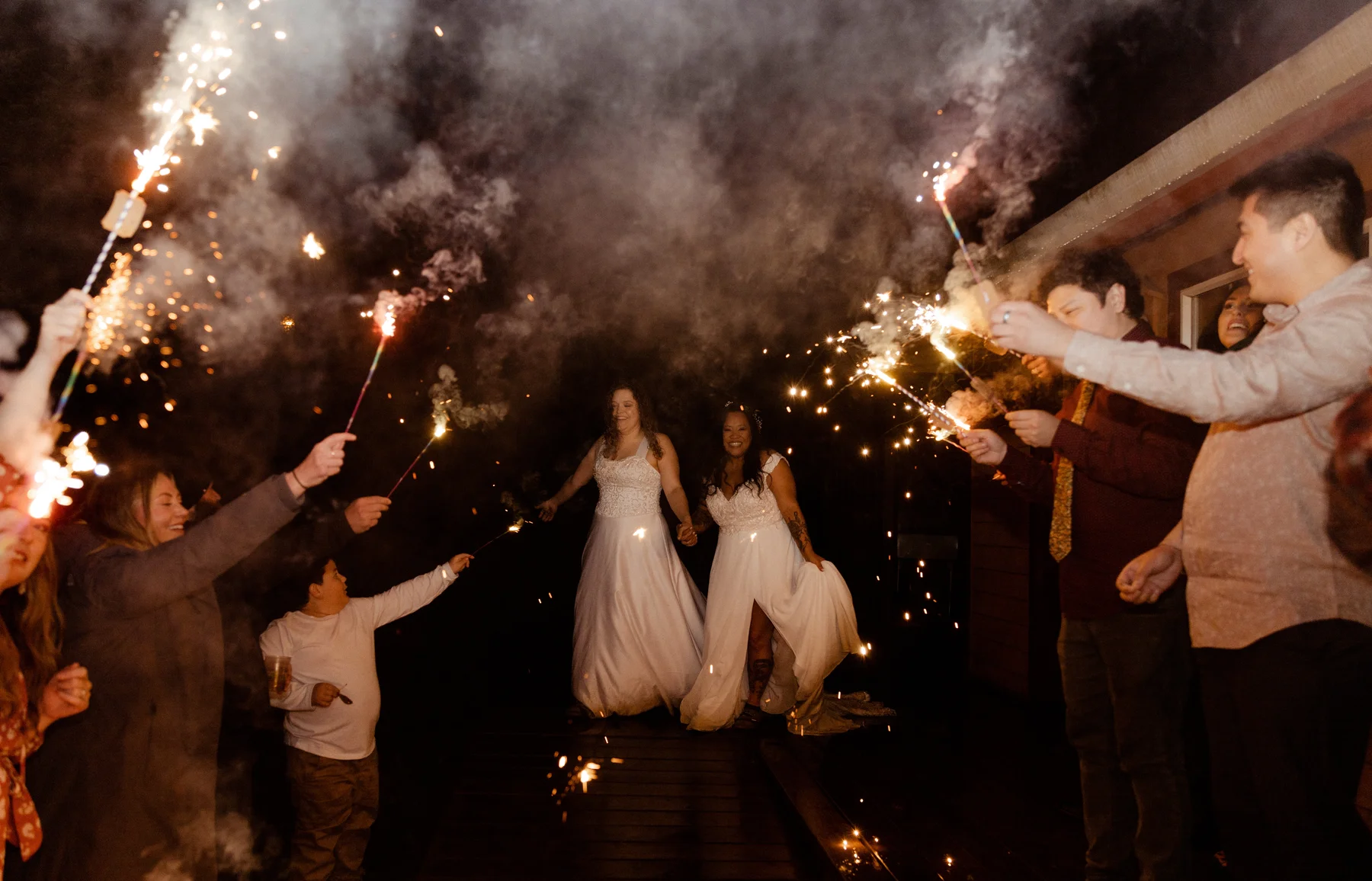 Brides Rachel and Jamie Snow walk hand-in-hand through a sparkler send-off tunnel with guests at Yachats Inn, Oregon.