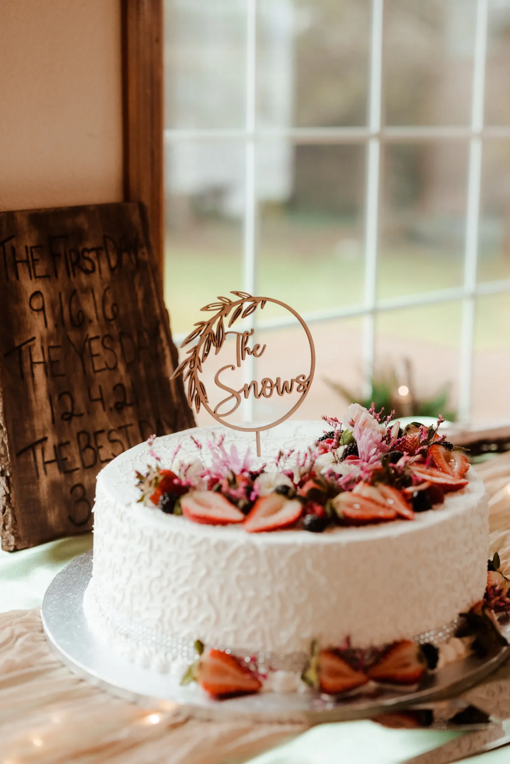 Wedding cake topped with 'The Snows' wooden topper and fresh berries and flowers at Yachats Inn in Oregon.