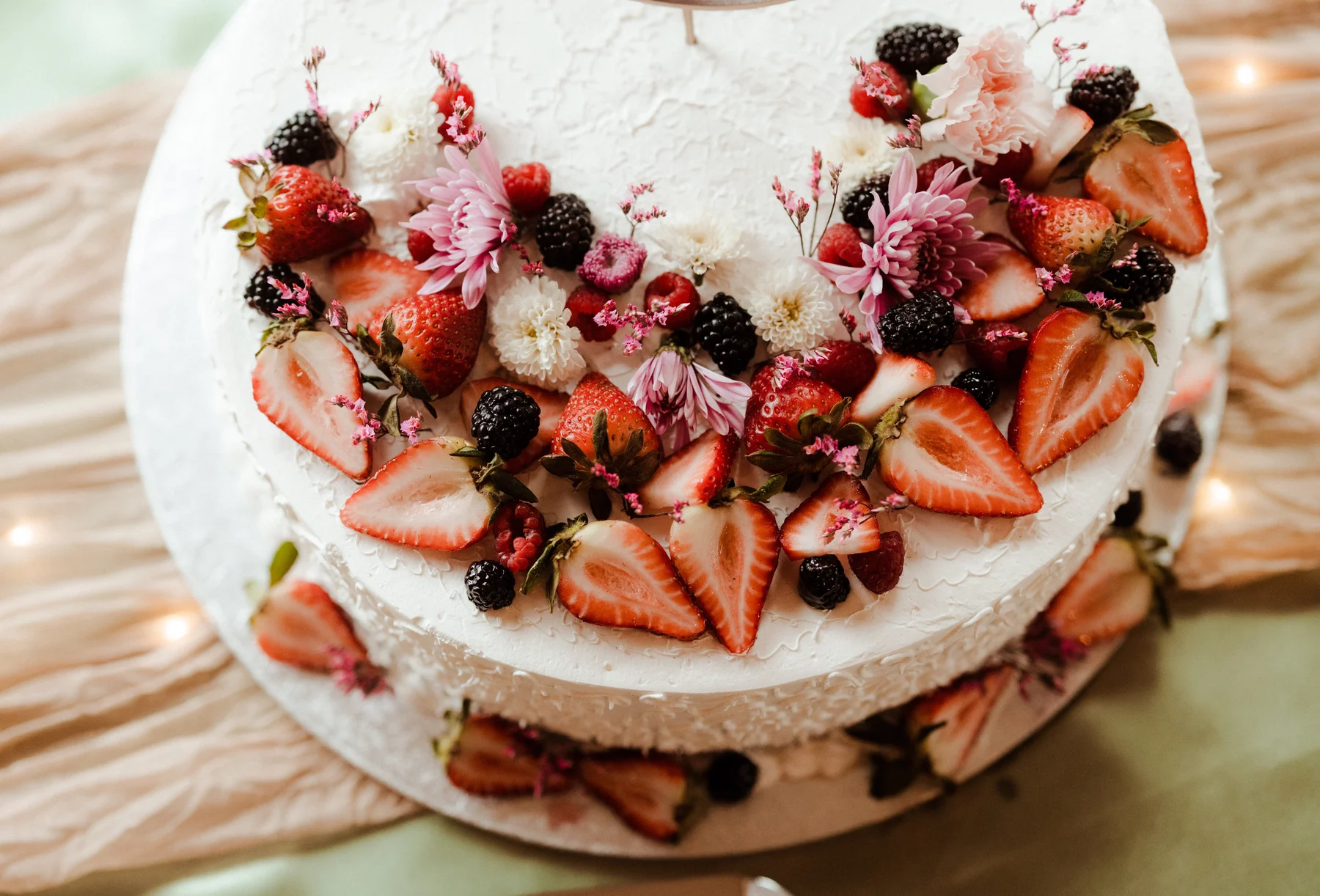 A white two-tiered wedding cake adorned with fresh strawberries, blackberries, raspberries, and pink and white flowers at Yachats Inn.