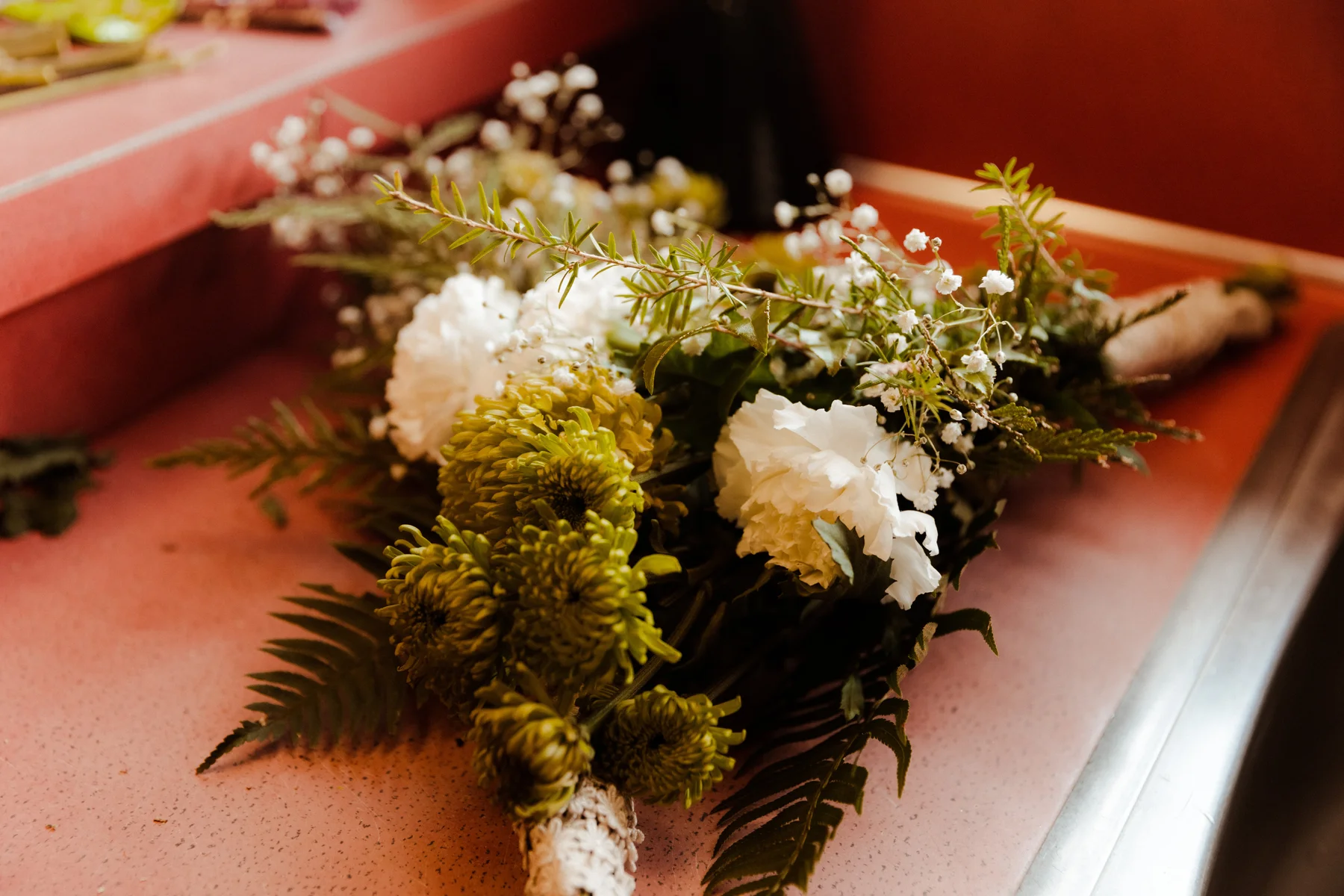 A bridal bouquet with green chrysanthemums, white carnations, baby's breath and ferns rests on a pink surface at Yachats Inn.