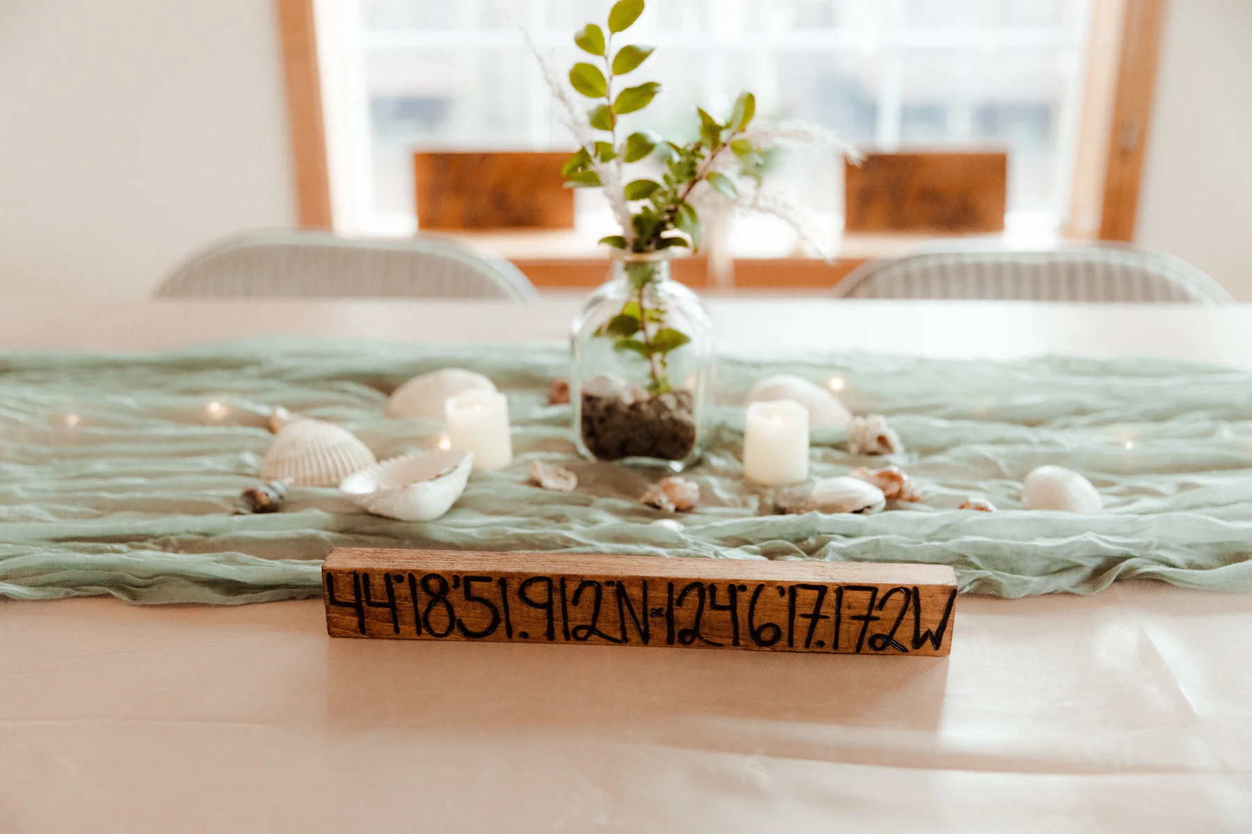 Coastal tablescape with GPS coordinates on a wood sign, seashells, candles and greenery at Yachats Inn in Oregon.