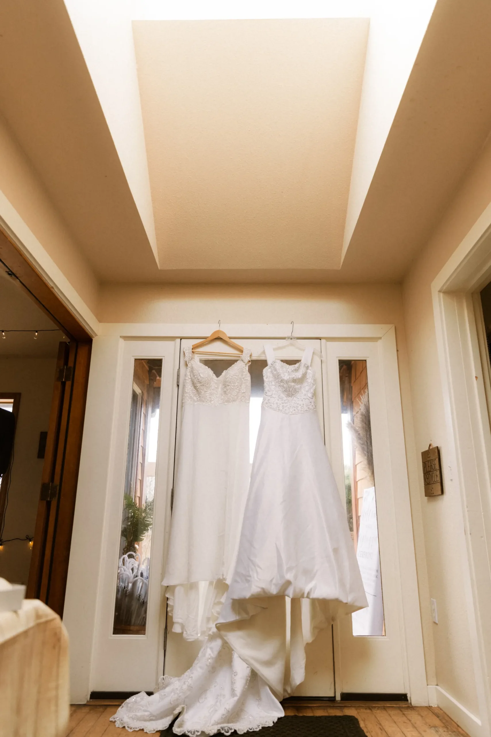 Two white wedding gowns hanging on a door at Yachats Inn in Oregon for Rachel and Jamie Snow's wedding.