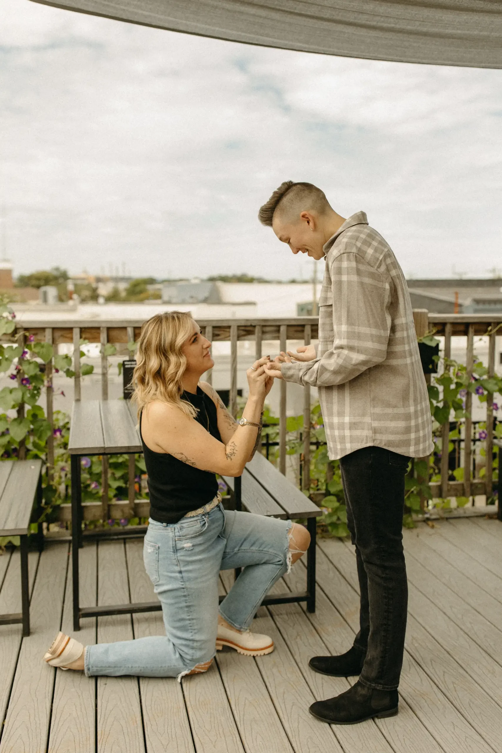 One of the partners kneels on a rooftop deck at Gravely Brewing Co in Denver, placing a ring on the other partner's hand.
