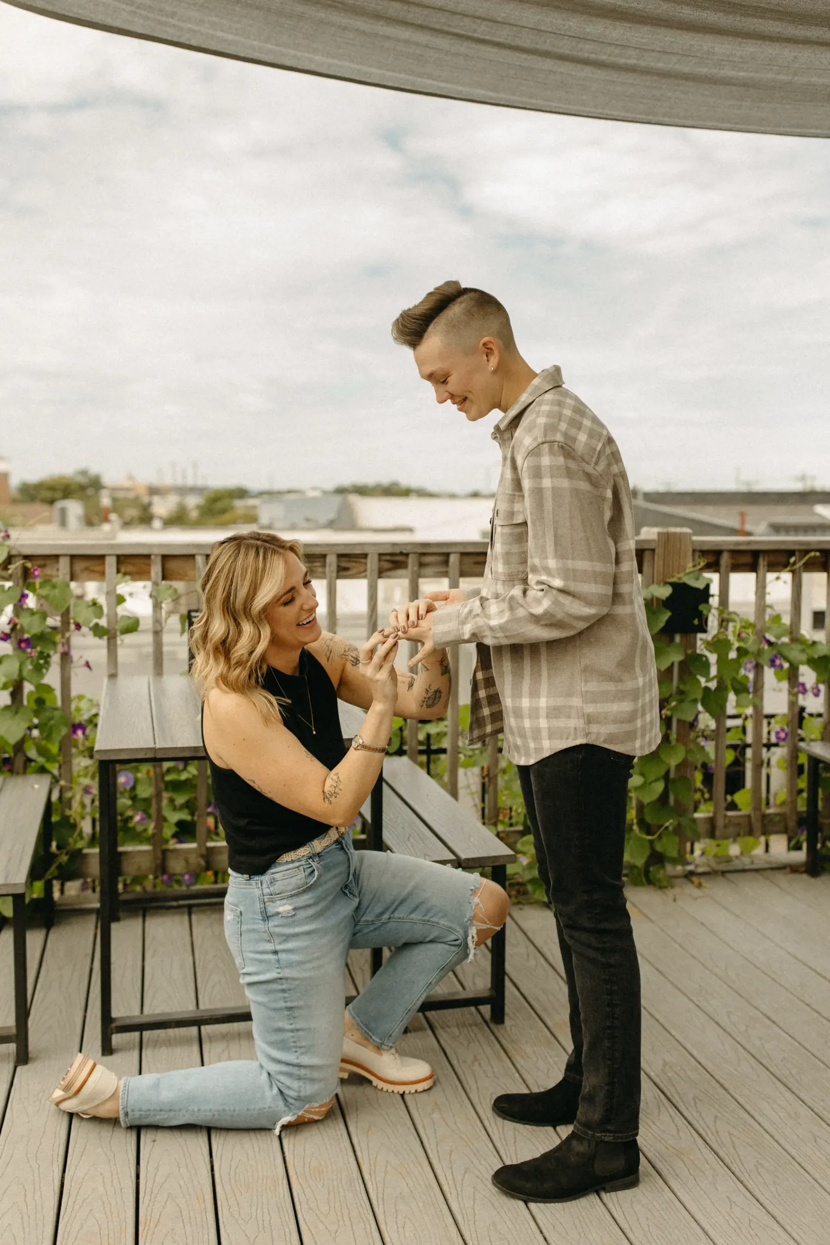 One of the partners kneels on a rooftop deck at Gravely Brewing Co in Denver, placing a ring on the other partner's finger.