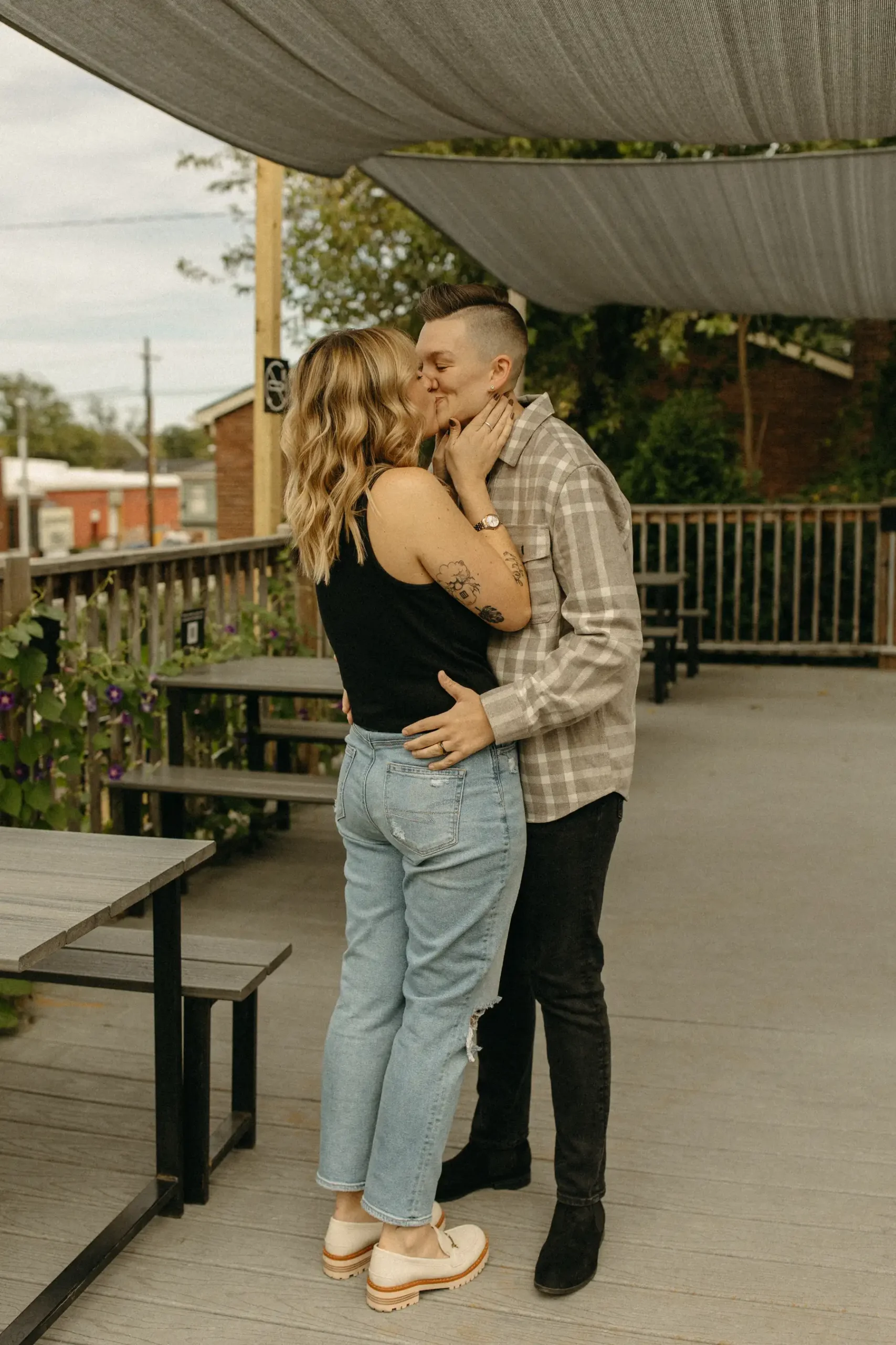 The couple shares a kiss on the outdoor deck at Gravely Brewing Co in Denver, Colorado, during their engagement session.