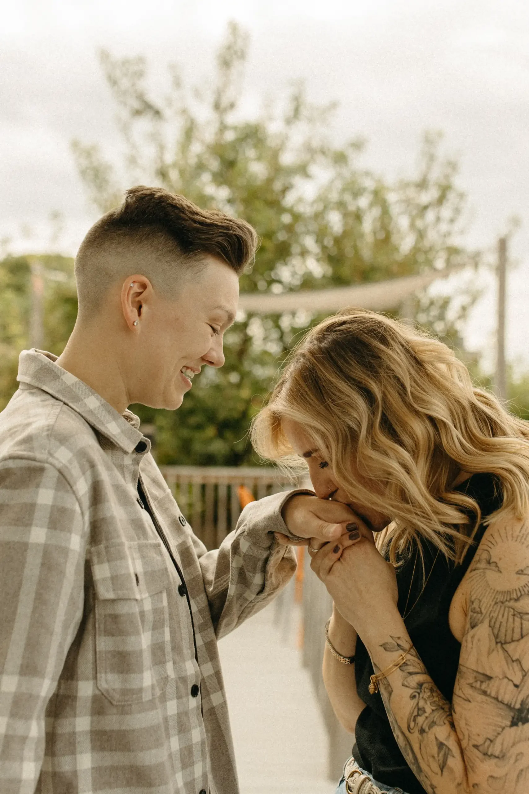 One of the partners kisses the other's hand while they laugh together during their engagement session at Gravely Brewing Co in Denver.