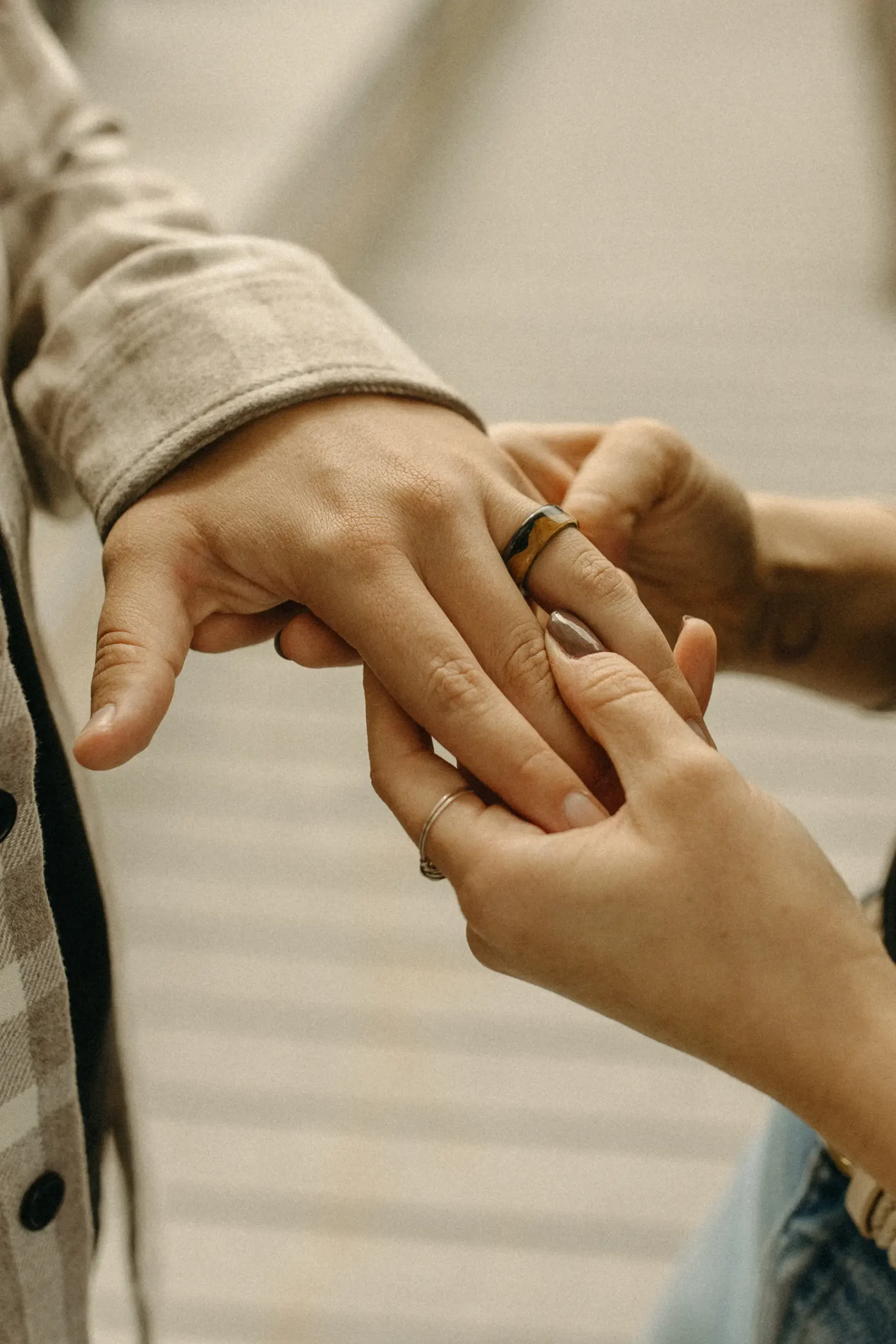 One of the partners slides a wood-and-metal band onto the other's ring finger during their engagement session at Gravely Brewing Co in Denver.