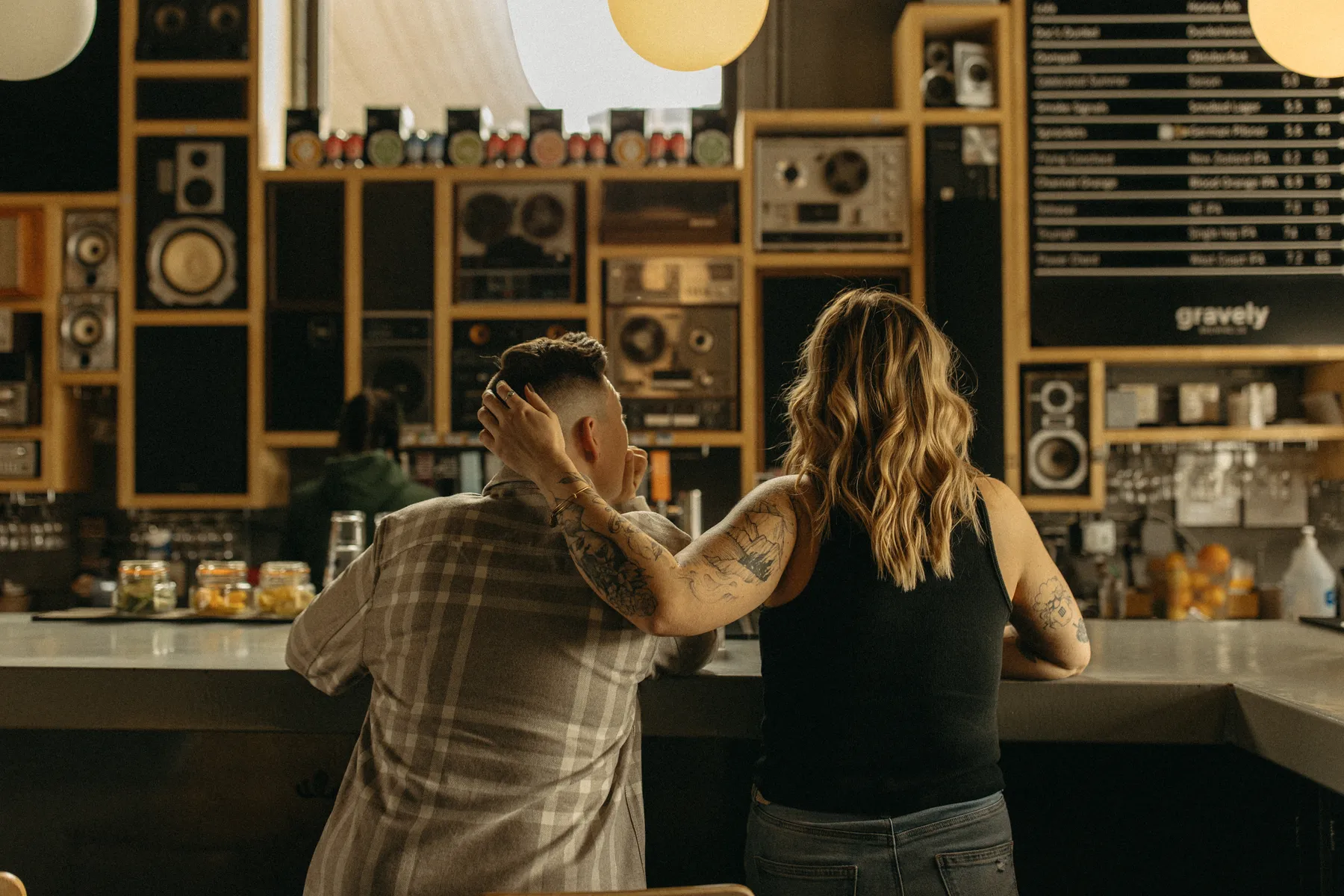 The couple leans against the bar at Gravely Brewing Co in Denver, Colorado, one partner resting an arm around the other.