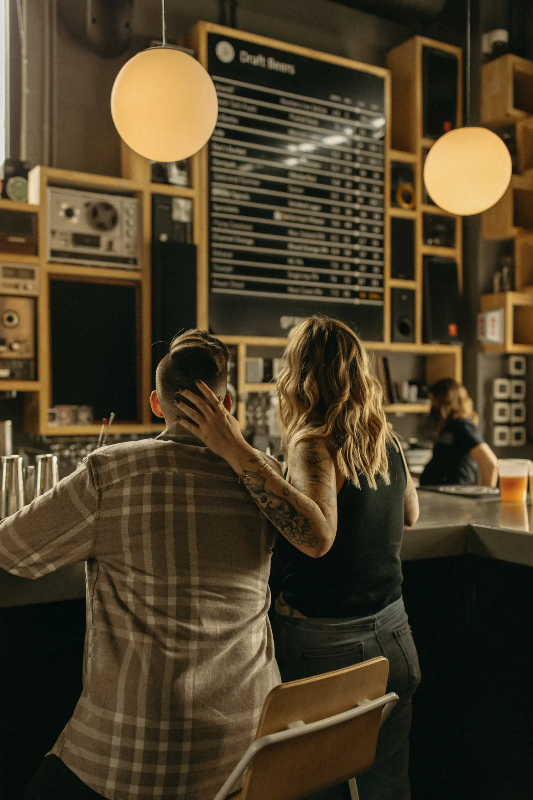 A couple leans together at the bar at Gravely Brewing Co in Denver, Colorado, one partner resting an arm around the other while they review the draft beer menu.