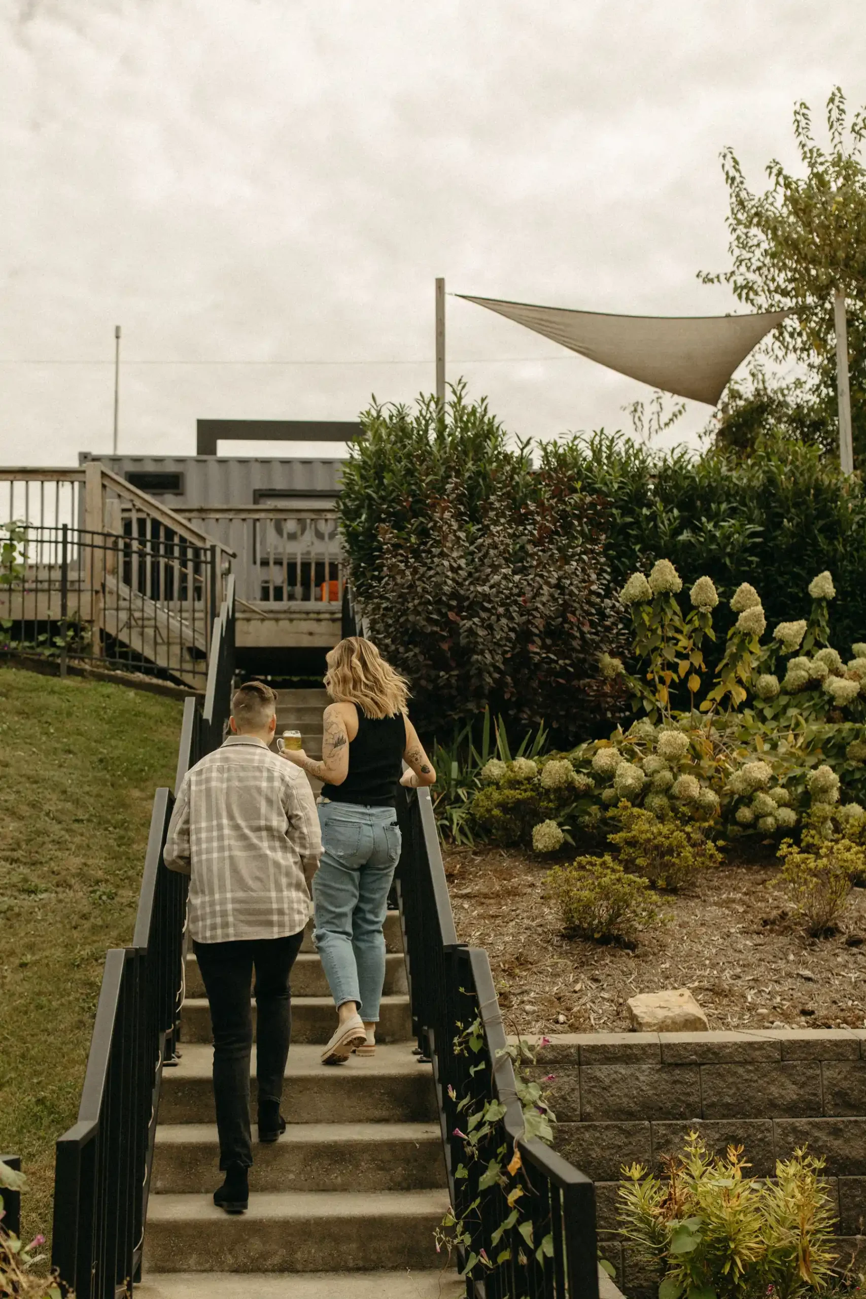 The couple walks up outdoor stairs at Gravely Brewing Co in Denver, Colorado, surrounded by lush garden landscaping.