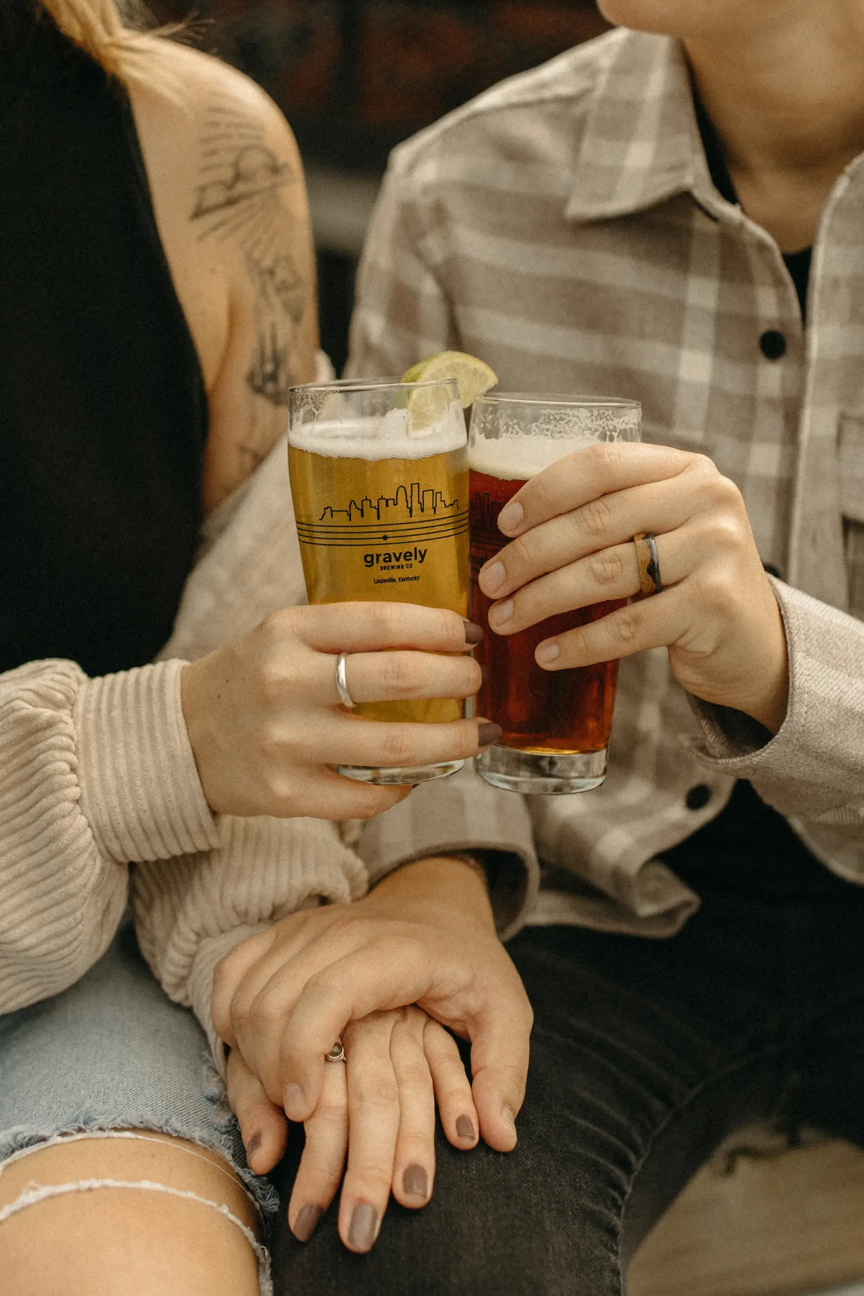 The couple clinks pint glasses of beer at Gravely Brewing Co in Louisville, Kentucky, their hands intertwined.