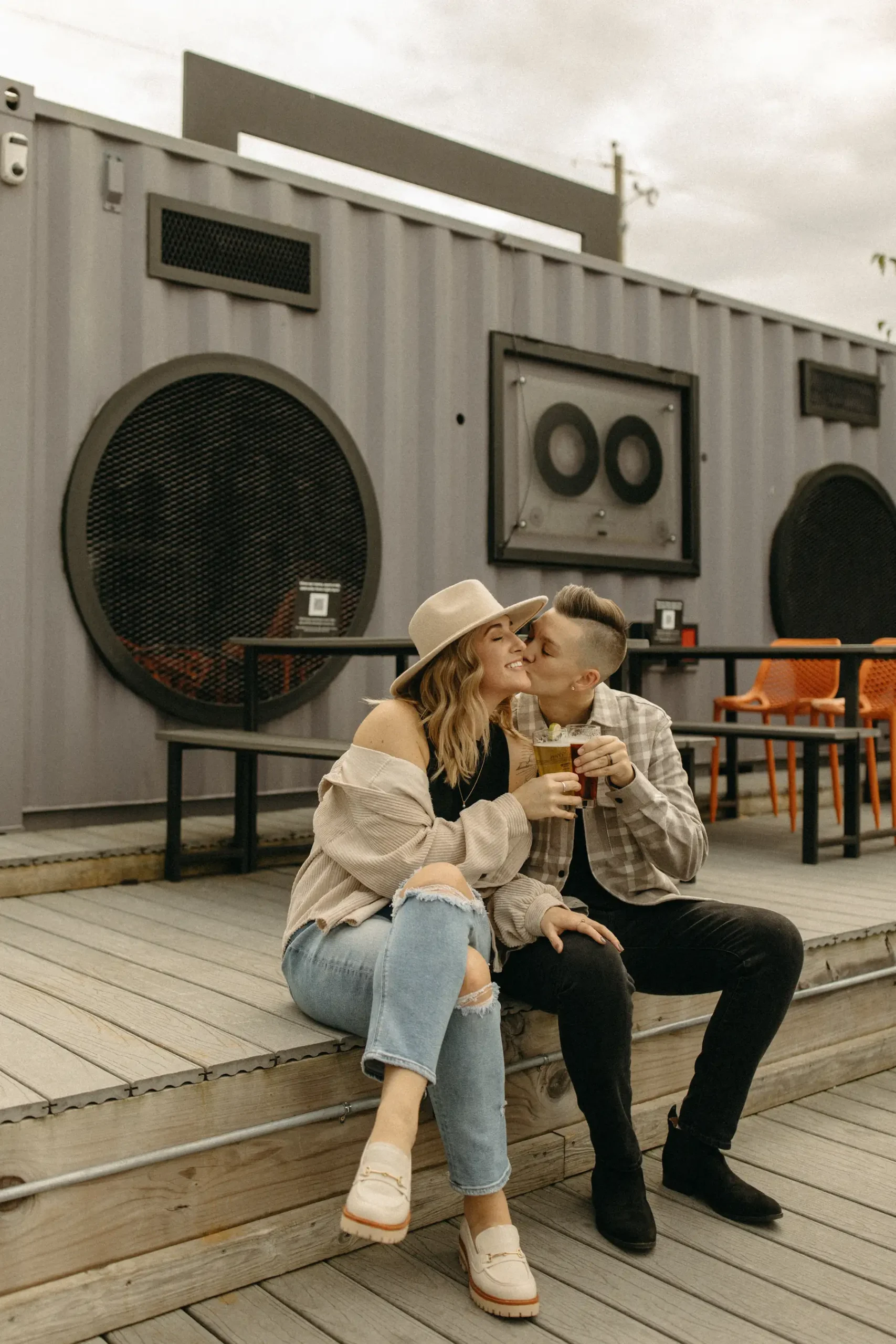 The couple shares a kiss while holding craft beers on the wooden deck at Gravely Brewing Co in Denver, Colorado.