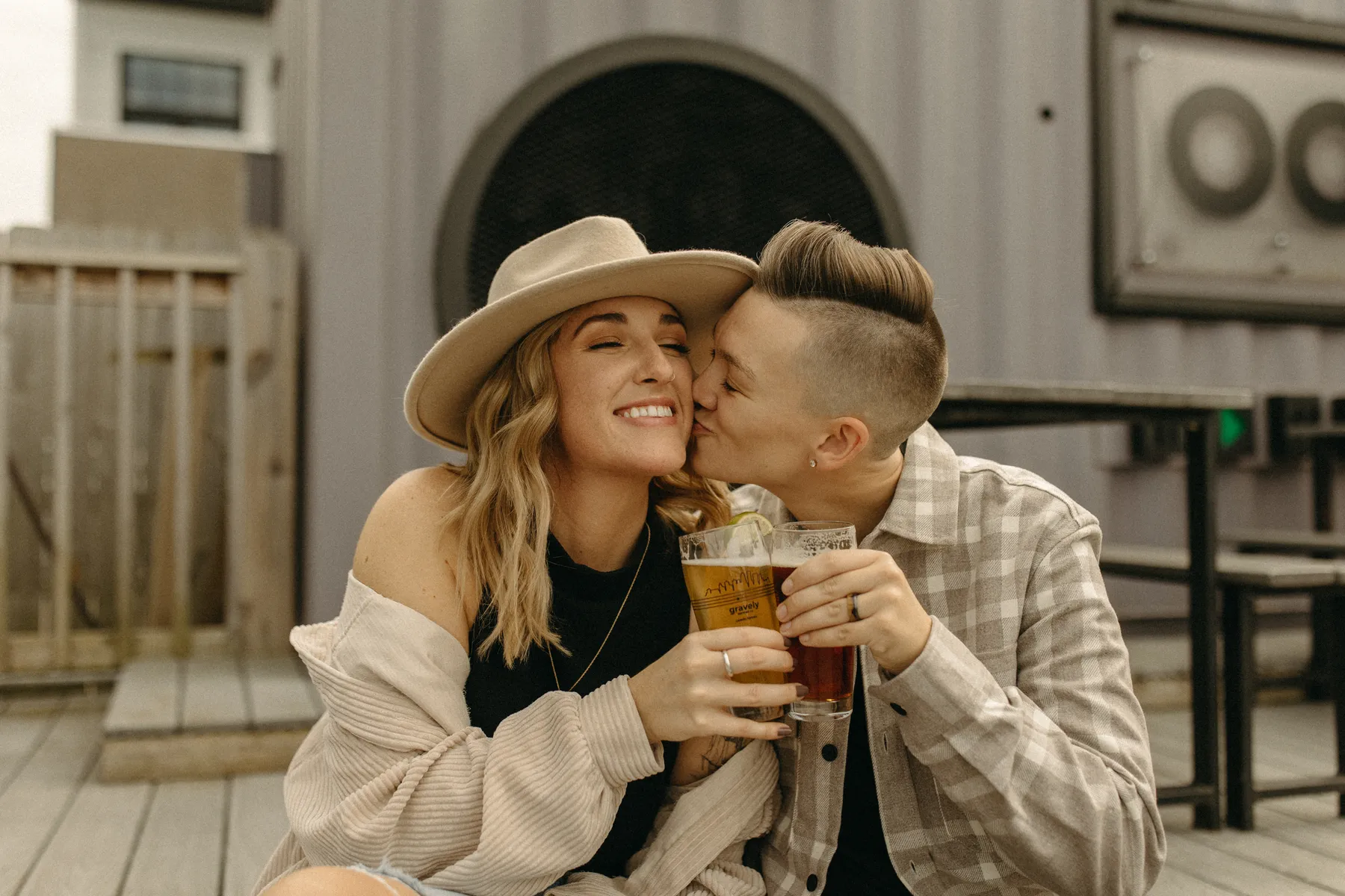 The couple shares a kiss and clinks beer glasses during their engagement session at Gravely Brewing Co in Denver, Colorado.