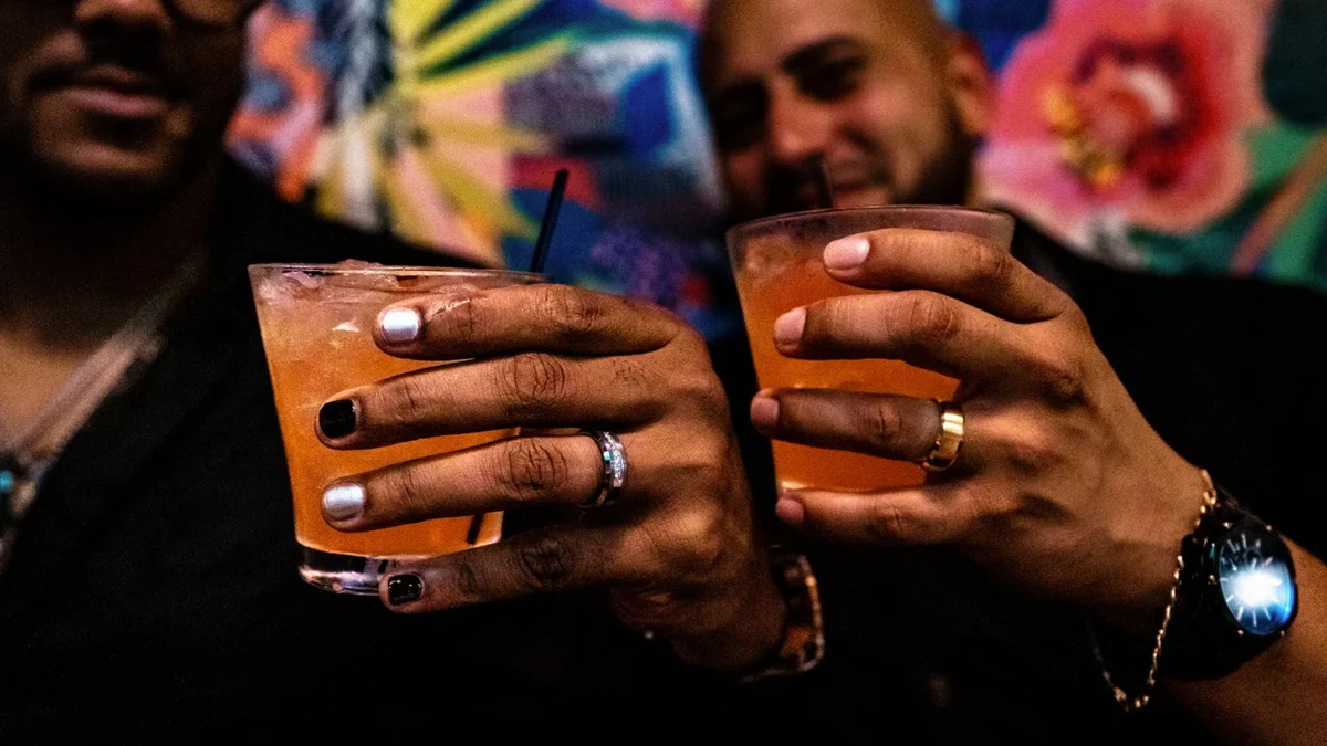 The couple clinks cocktail glasses at Our House in Goldsboro, NC, rings and a gold bracelet visible on their hands.