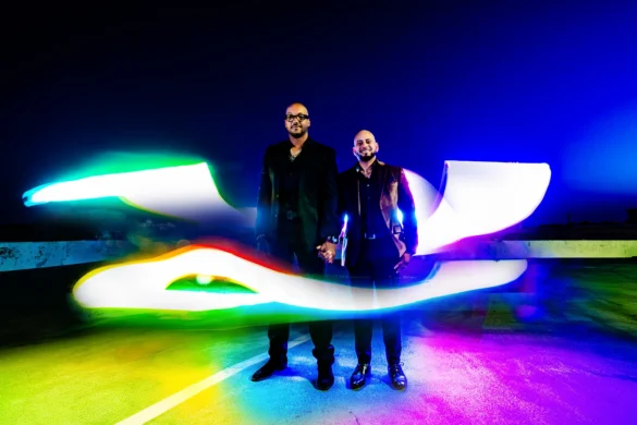 A couple holds hands on a rooftop in Goldsboro, NC, surrounded by vibrant light painting trails in rainbow colors.