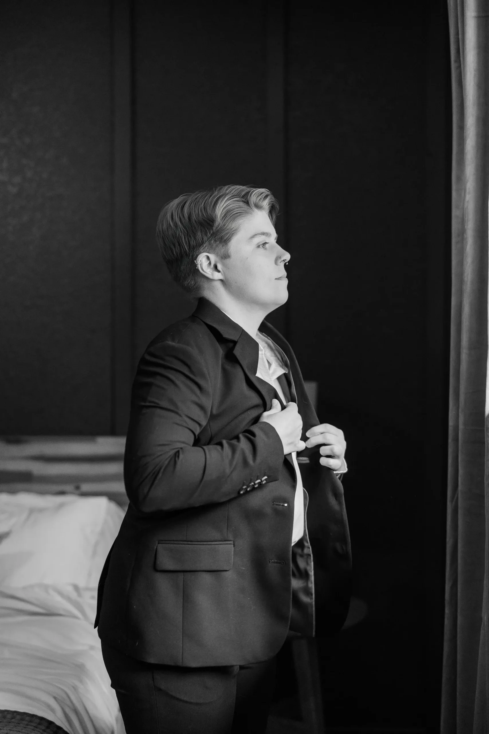 A person in a dark suit buttons their jacket while getting ready at Halfway House in Boulder, CO.
