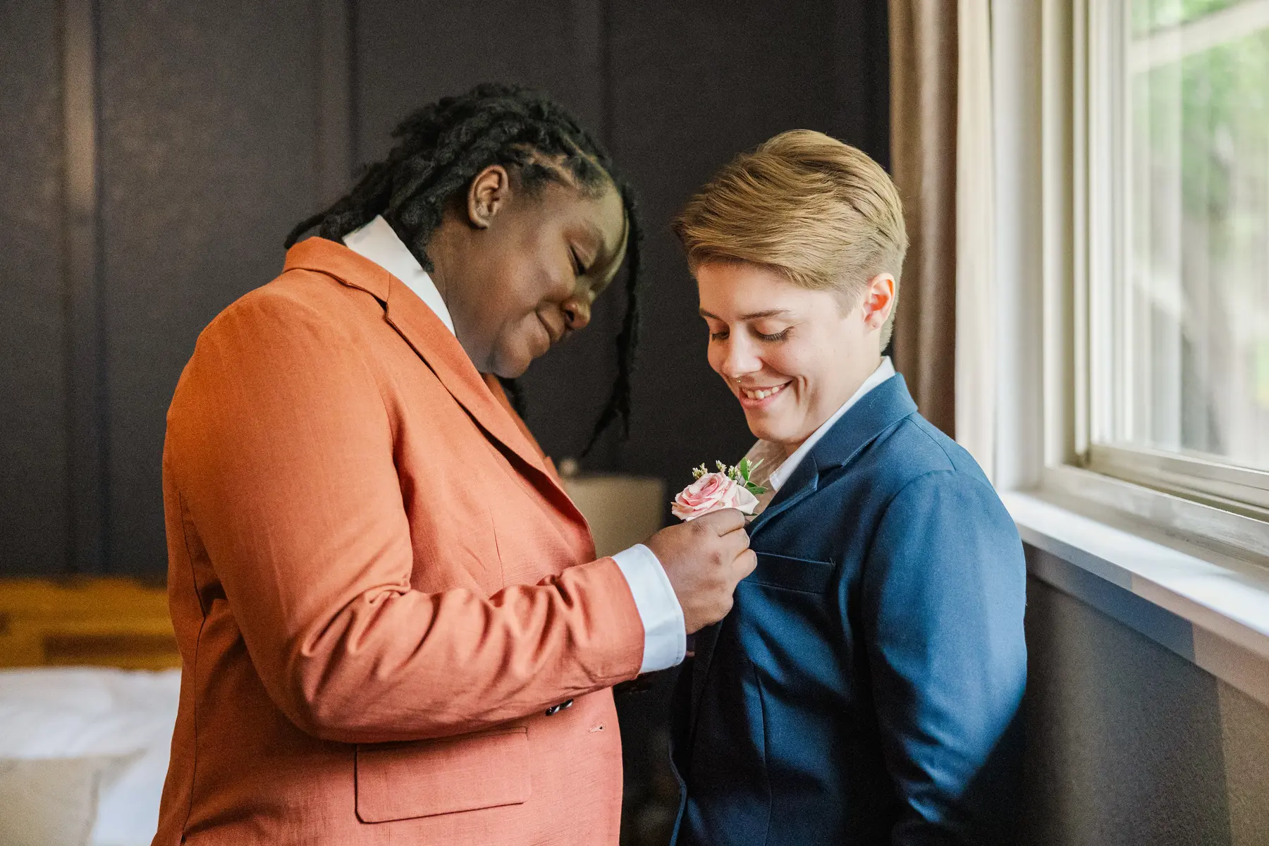Sydney and Hannah Rusow pin a boutonniere before their wedding at Halfway House in Boulder, CO.