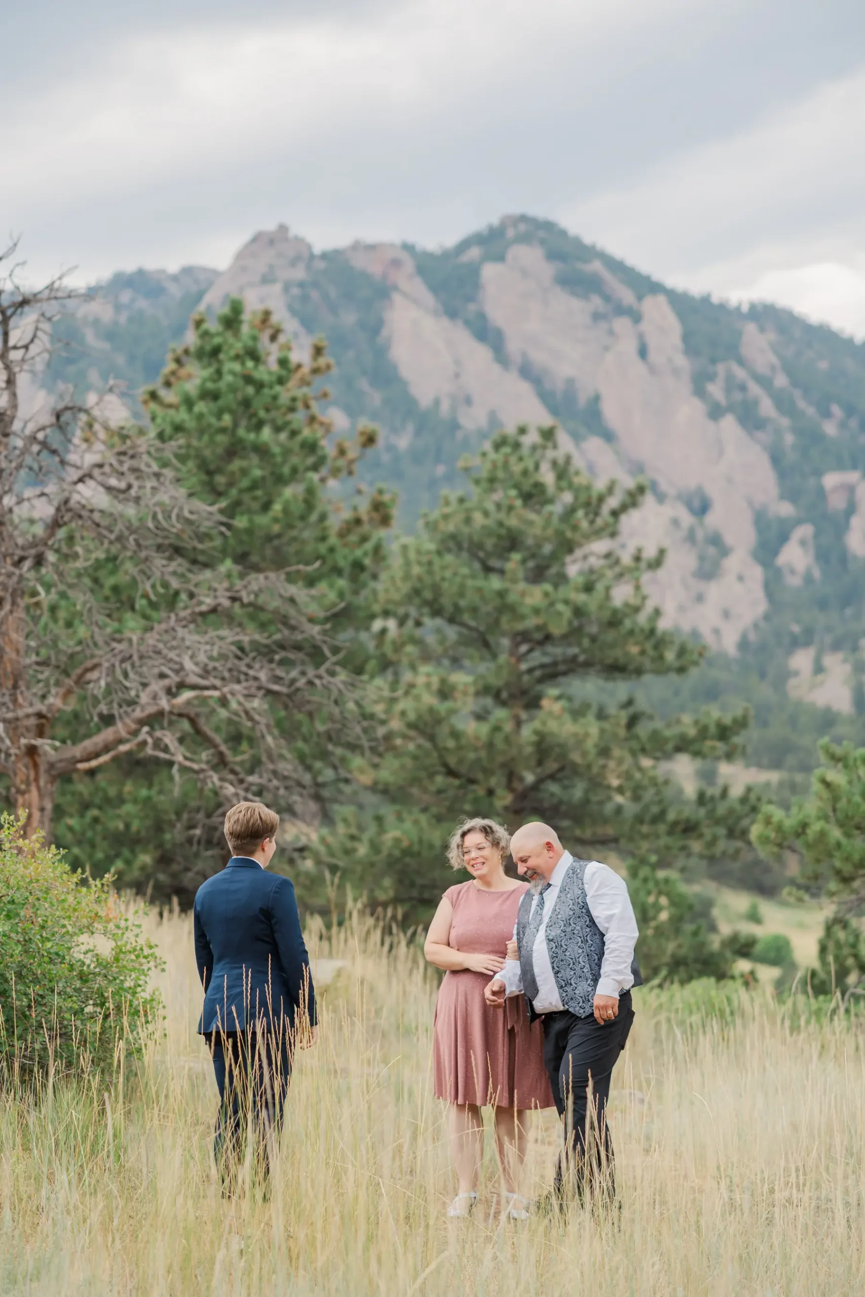 Sydney and Hannah Rusow share a joyful moment with an officiant in a mountain meadow at Halfway House in Boulder, CO.