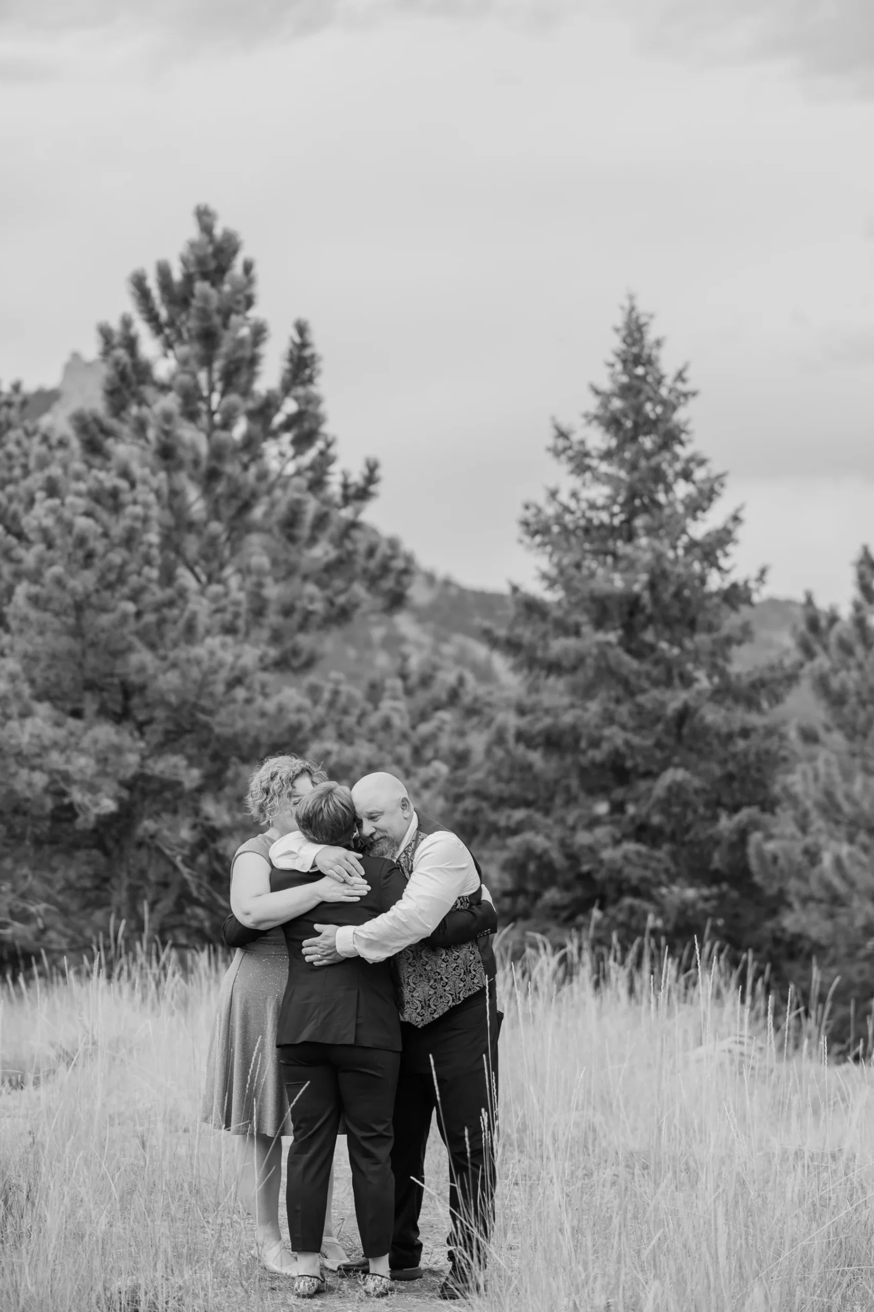 Sydney Rusow, Hannah Rusow, and a guest share an emotional group hug in a meadow at Halfway House in Boulder, CO.