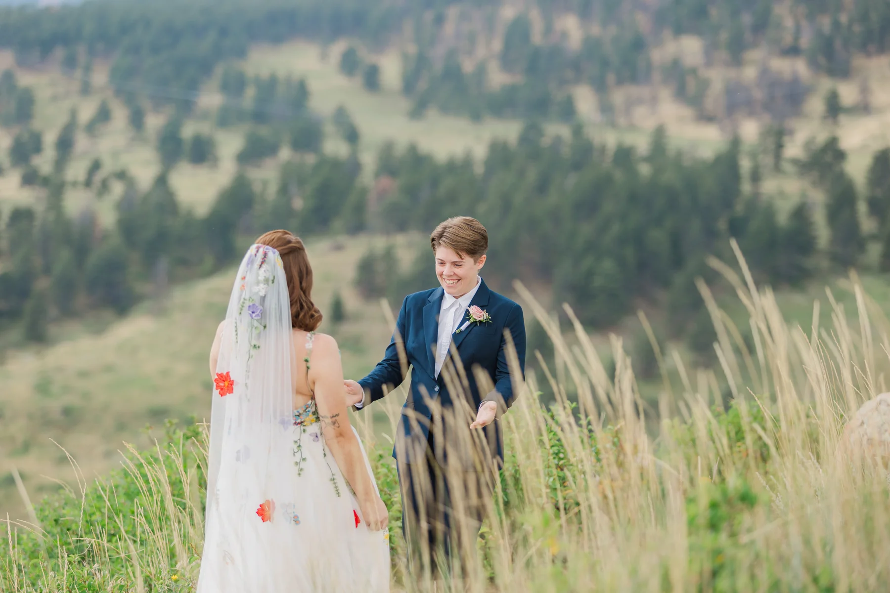 Sydney and Hannah Rusow share a joyful first look in a wildflower meadow at Halfway House in Boulder, CO.