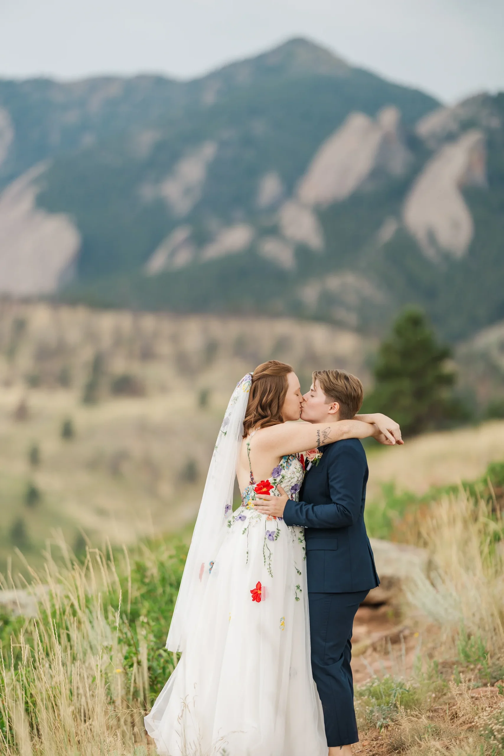Sydney and Hannah Rusow share a first kiss in floral gown and navy suit at Halfway House in Boulder, CO.
