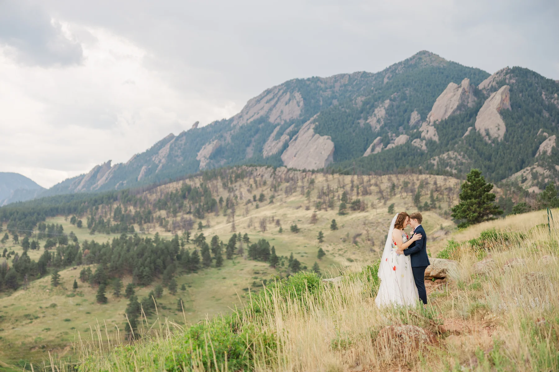 Sydney and Hannah Rusow embrace on a hillside with the iconic Flatirons mountains behind them in Boulder, CO.