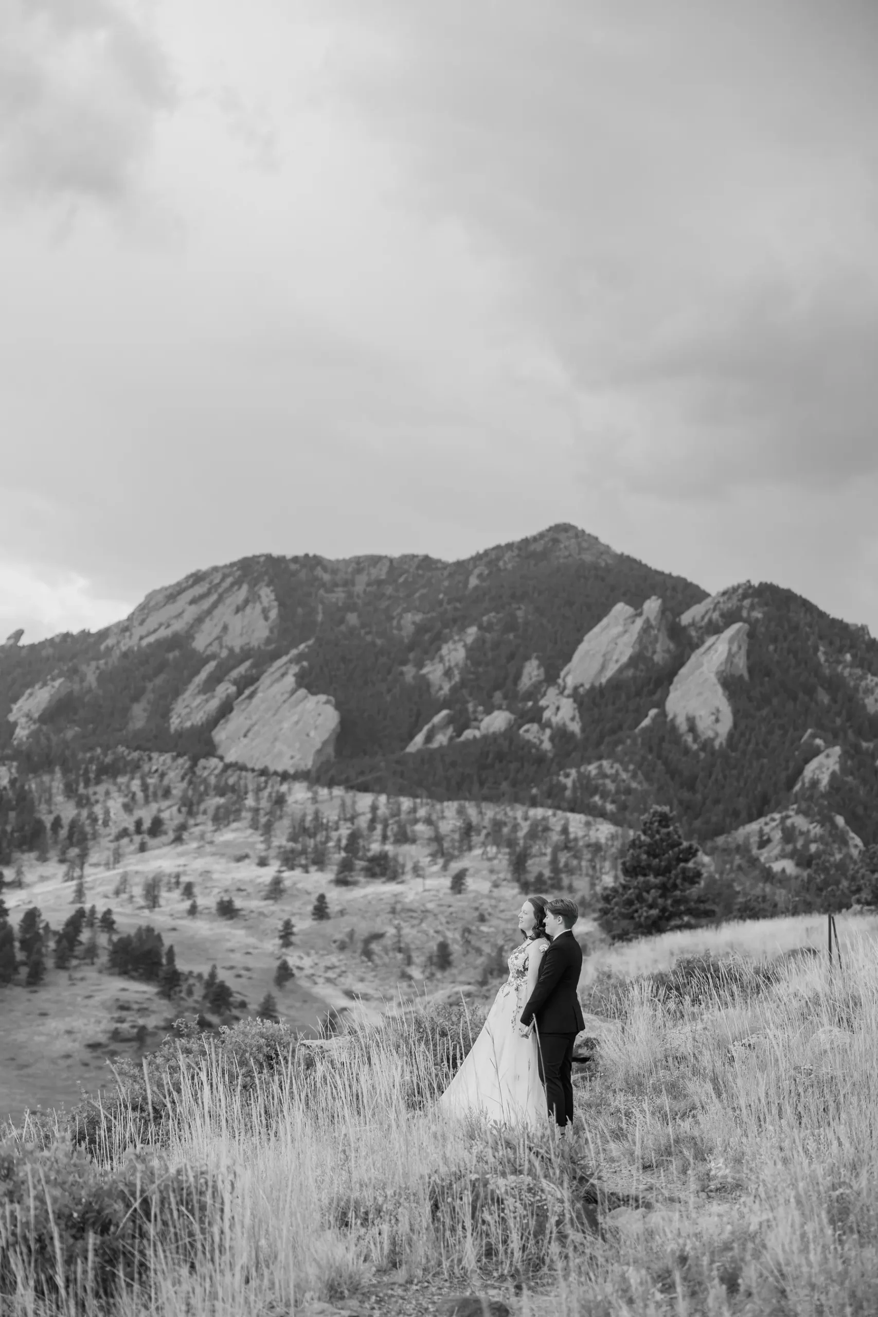 Sydney and Hannah Rusow stand together in a grassy meadow with the Flatirons rising behind them at Halfway House in Boulder, CO.