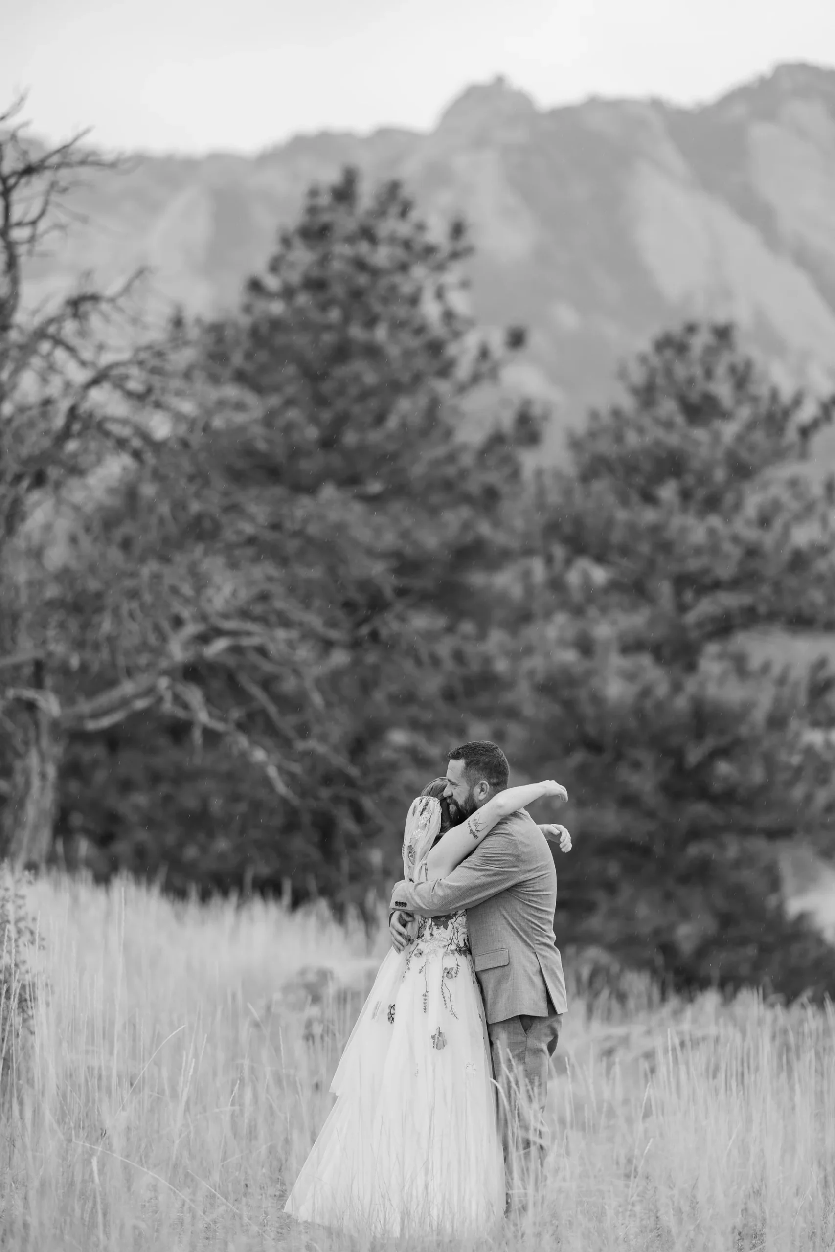 Sydney and Hannah Rusow embrace in a field of tall grass with the Flatirons in the background at Halfway House in Boulder, CO.