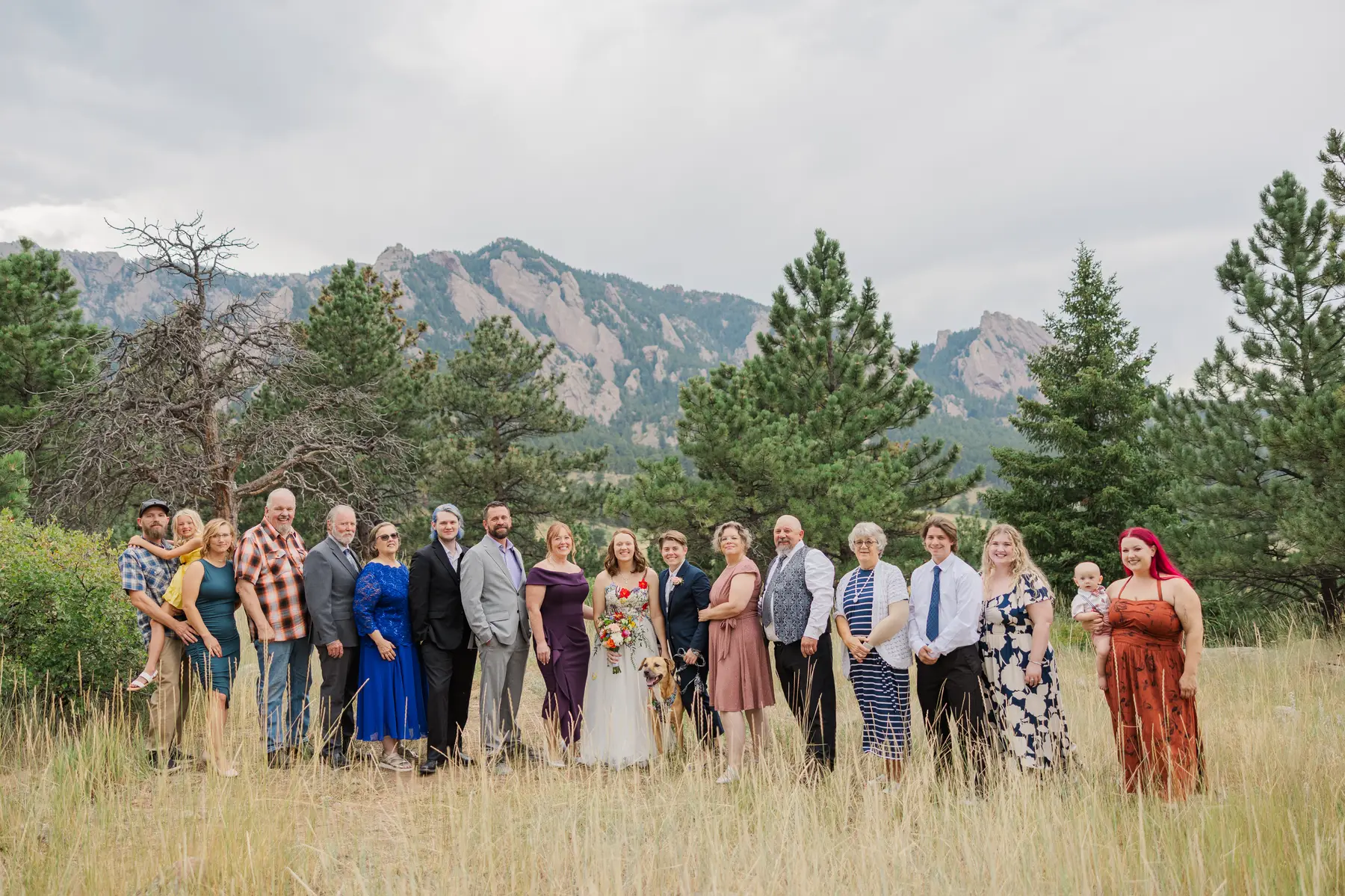 Sydney and Hannah Rusow pose with family and guests in a grassy meadow with the Flatirons in the background in Boulder, CO.