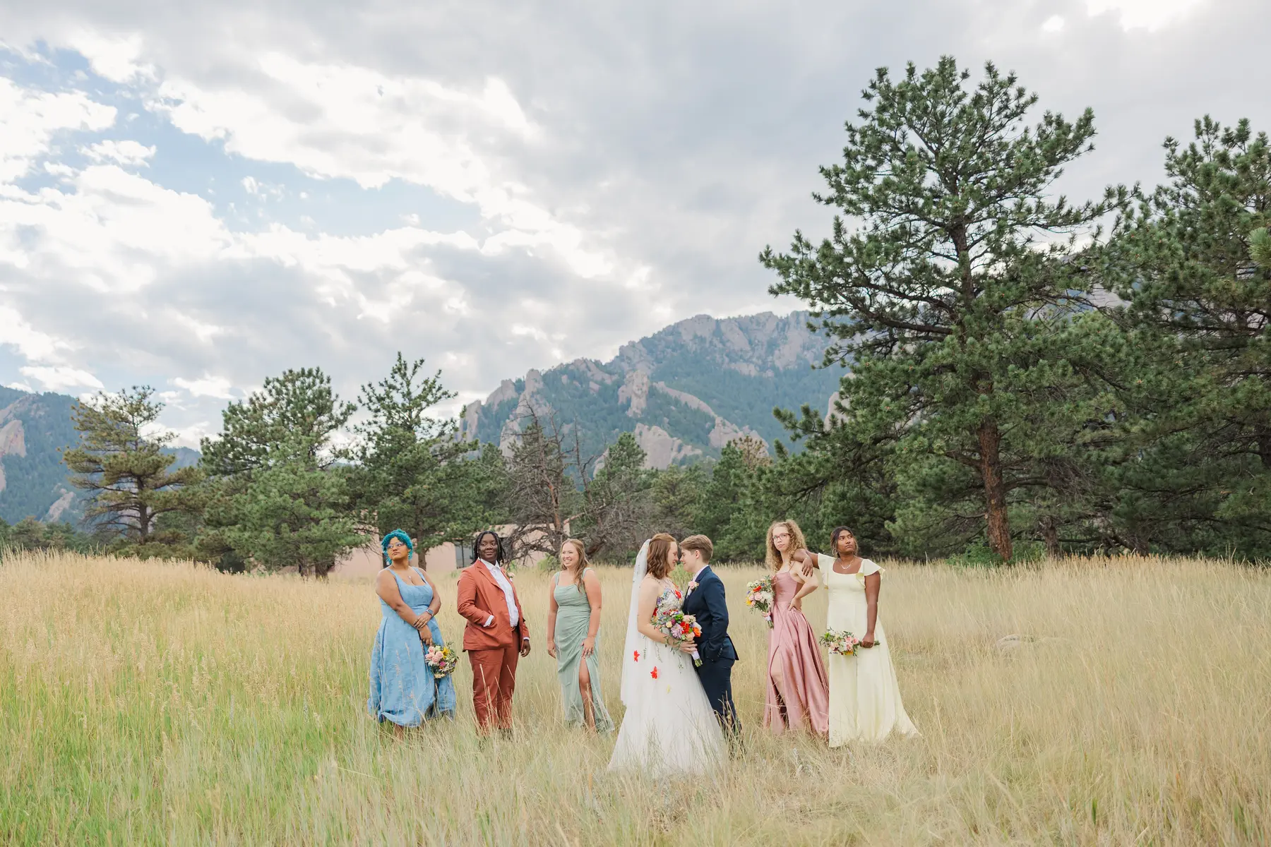 Sydney and Hannah Rusow share a moment with their wedding party in a golden meadow at Halfway House in Boulder, CO.