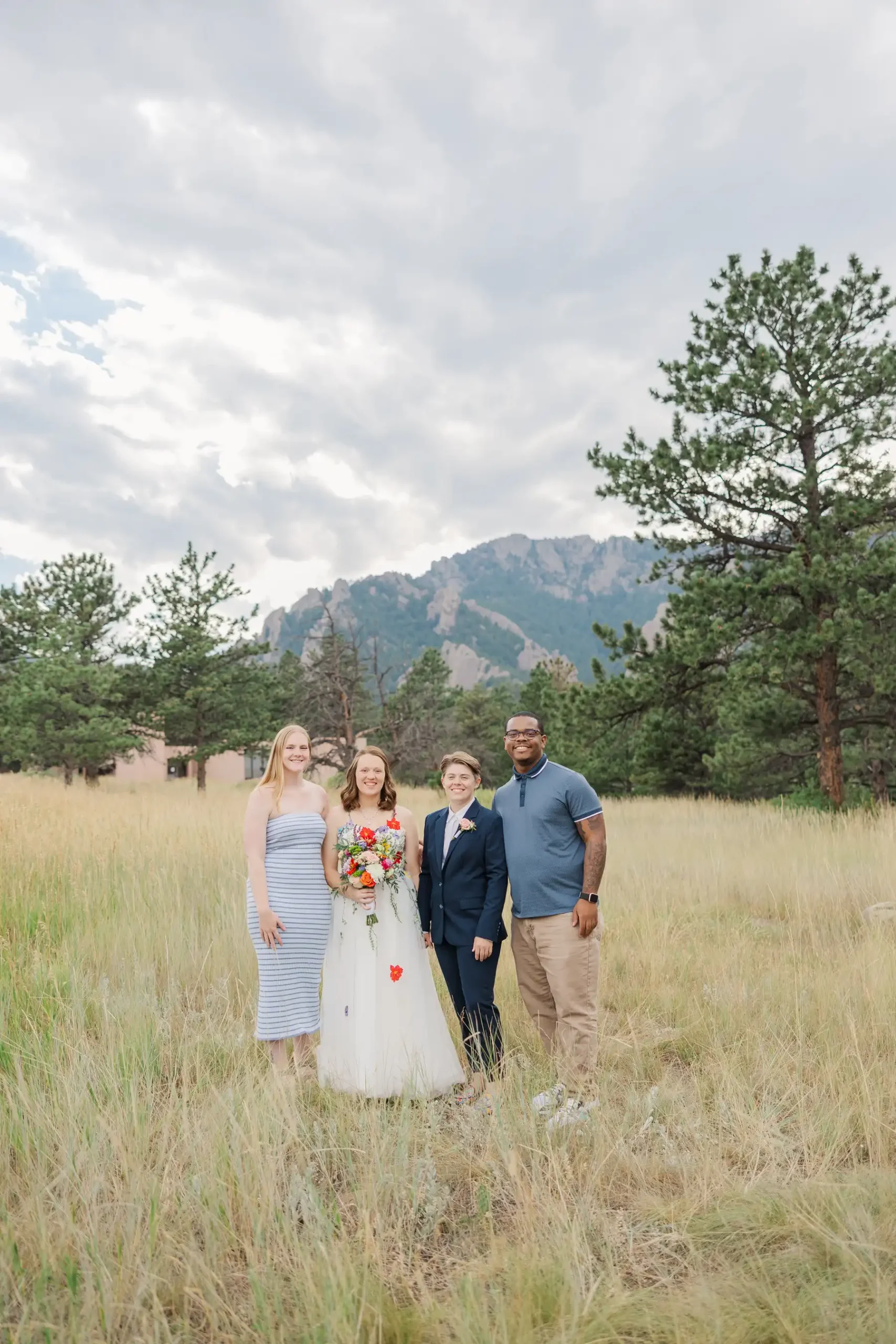 Sydney and Hannah Rusow pose with two guests in a grassy field with the Flatirons in the background at Halfway House in Boulder, CO.