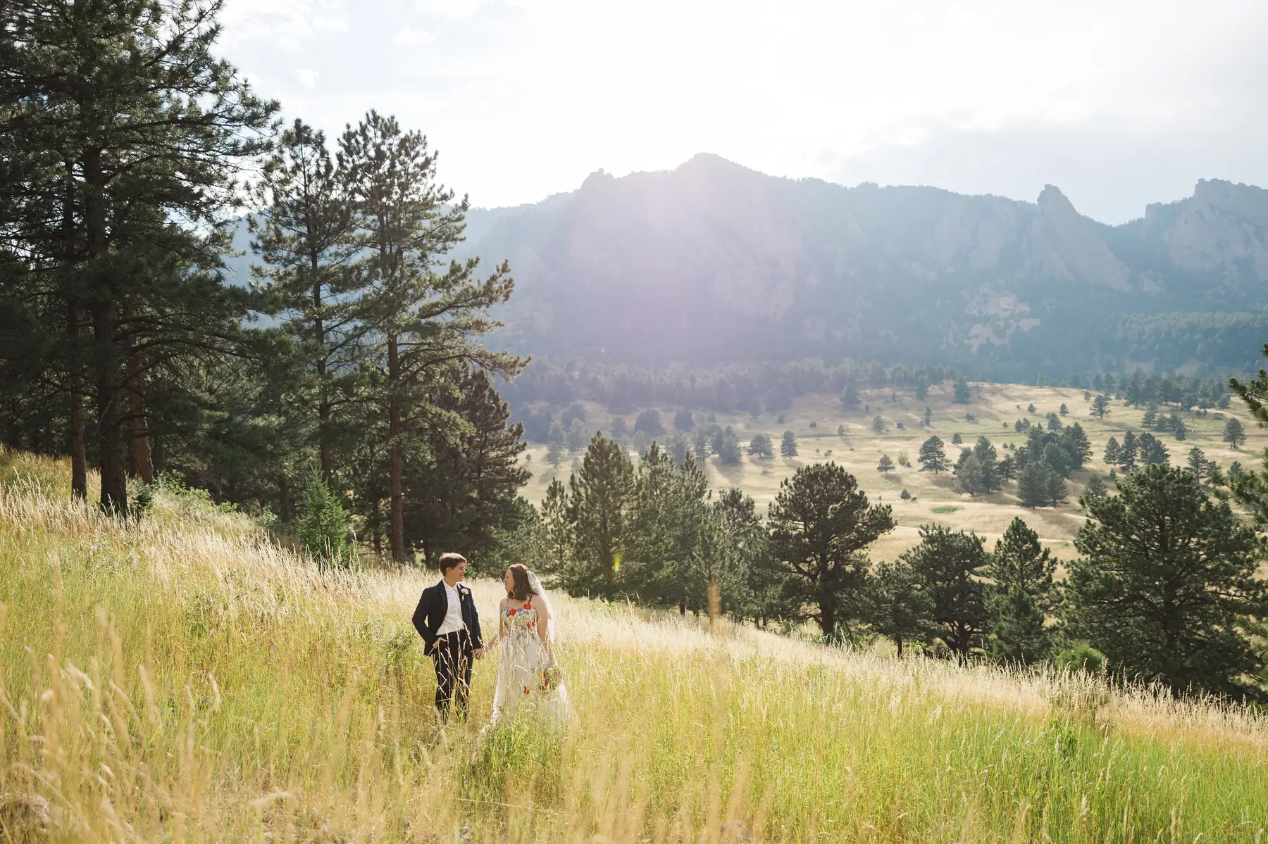 Sydney and Hannah Rusow walk hand in hand through a sunlit mountain meadow at Halfway House in Boulder, CO.