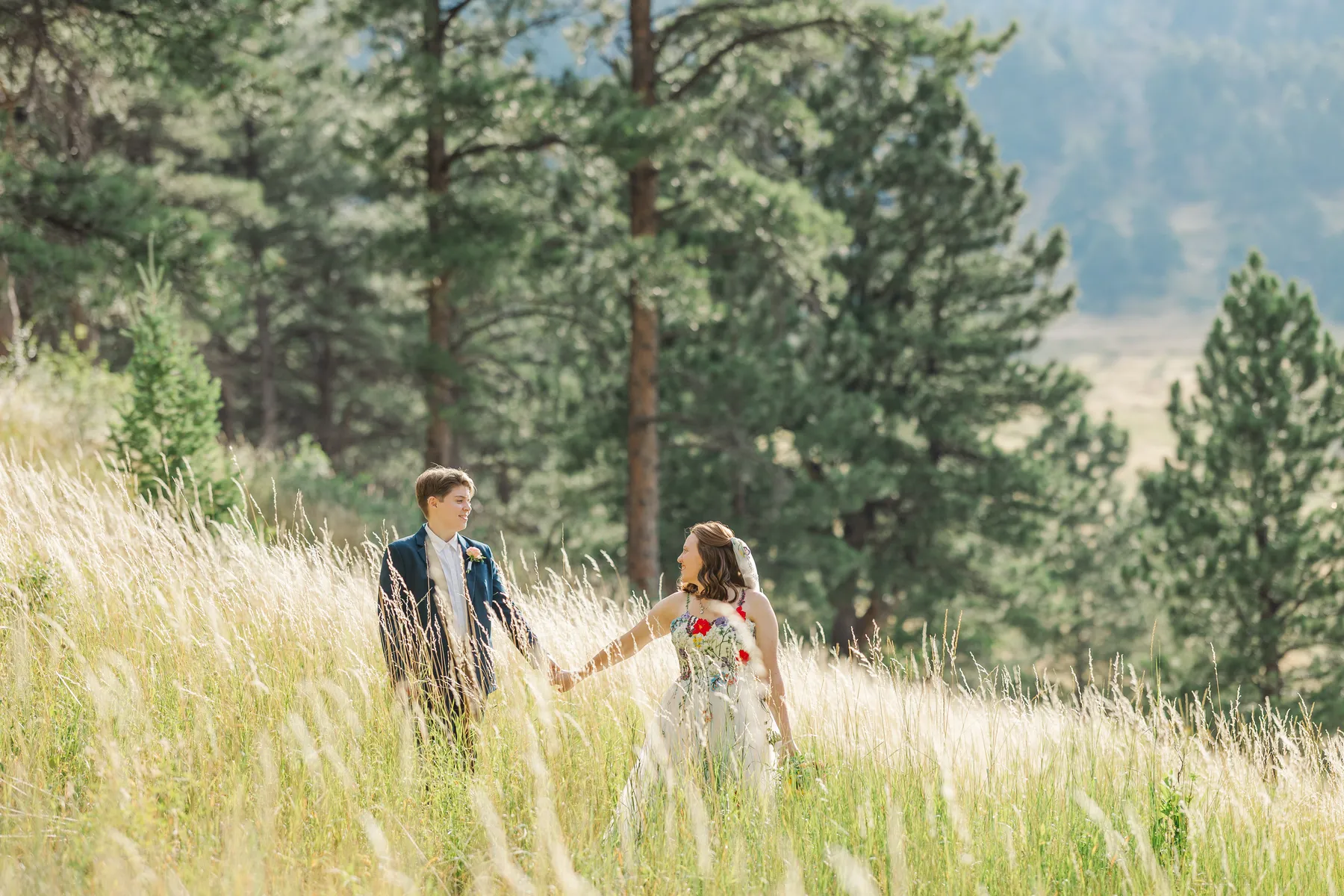 Sydney and Hannah Rusow walk hand-in-hand through a sunlit meadow at Halfway House in Boulder, CO.