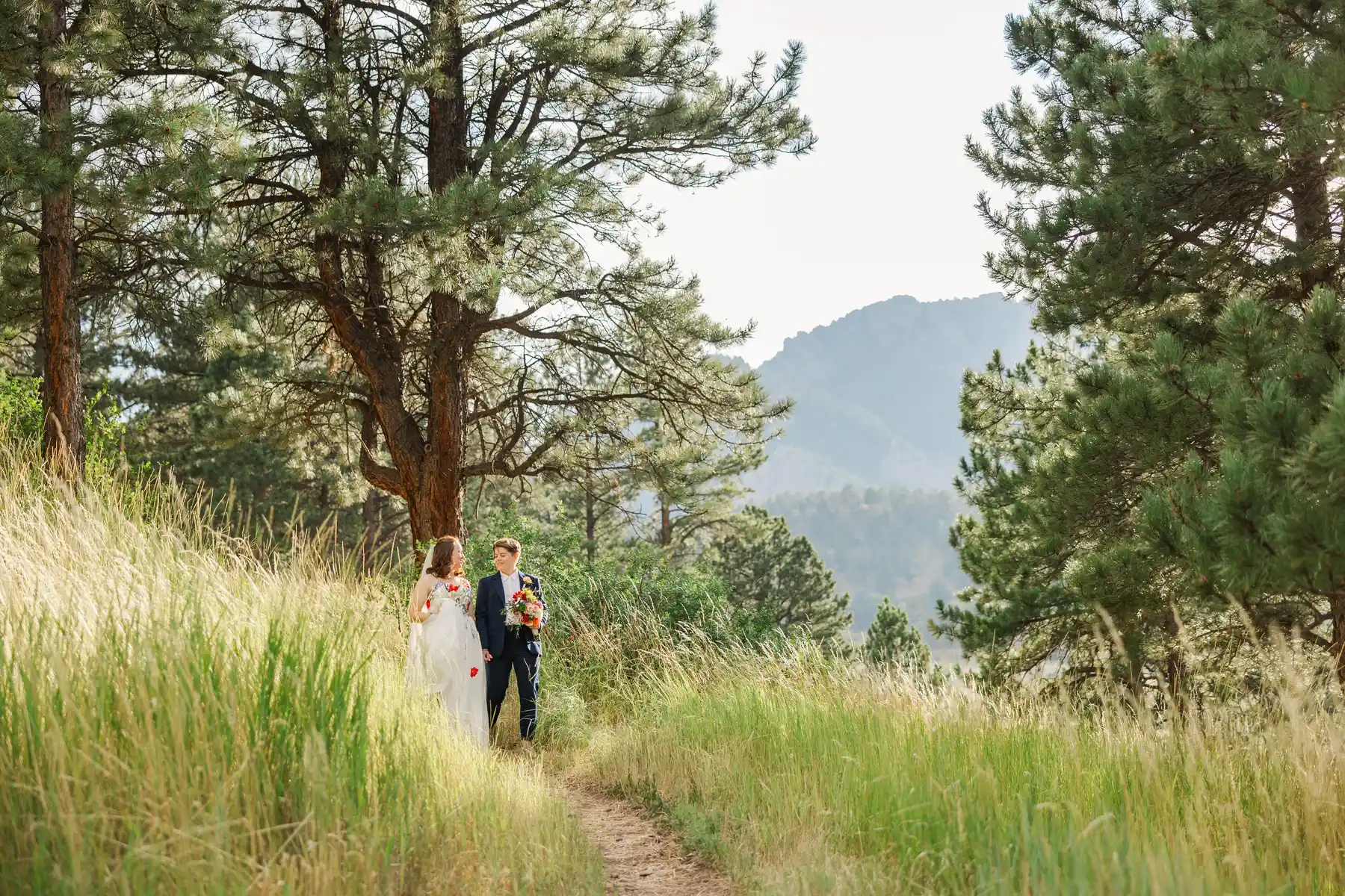 Sydney and Hannah Rusow walk a mountain trail at Halfway House in Boulder, CO, surrounded by pines and wildflasses.