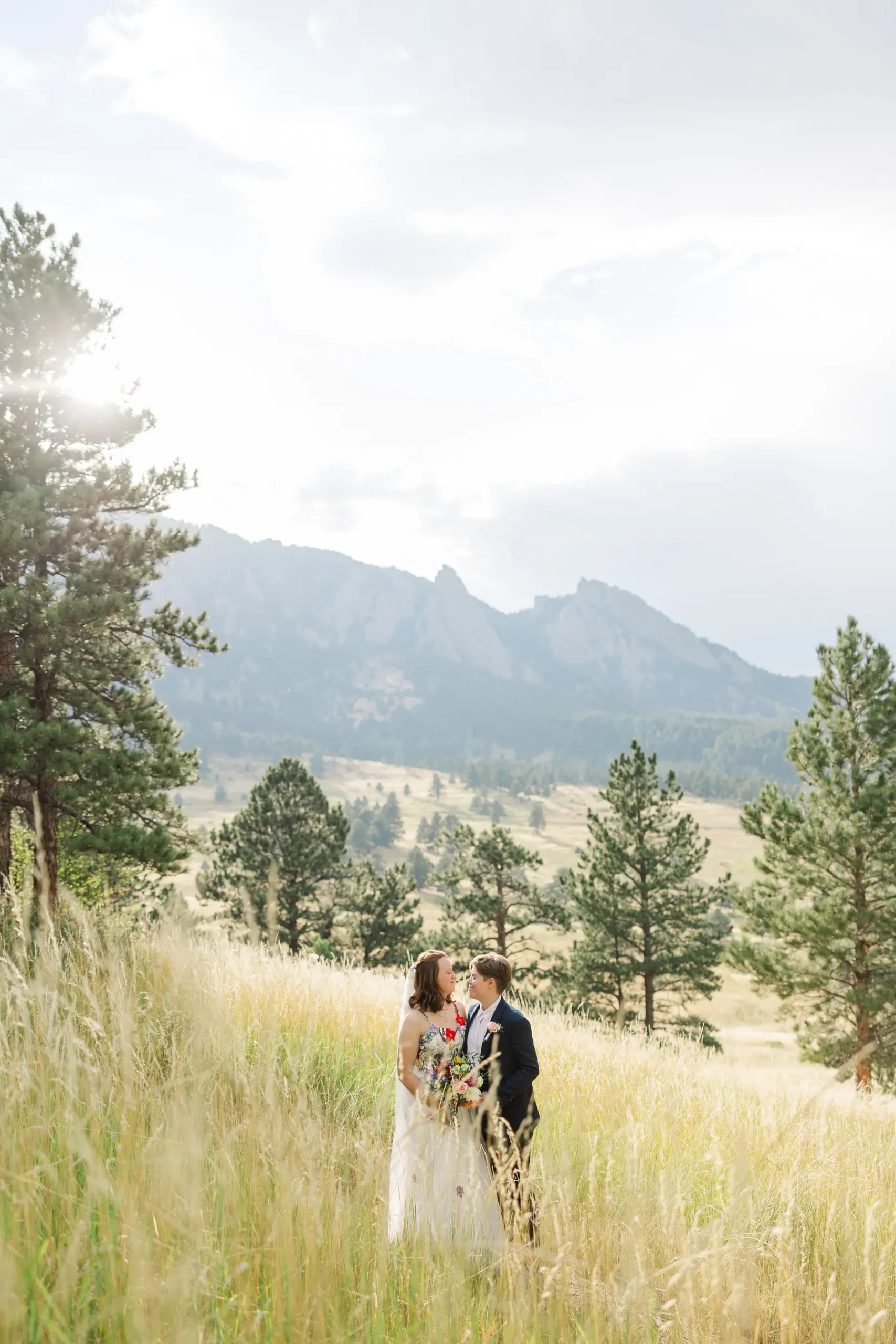 Sydney and Hannah Rusow stand together in a golden meadow with the Flatirons mountains behind them at Halfway House in Boulder, CO.