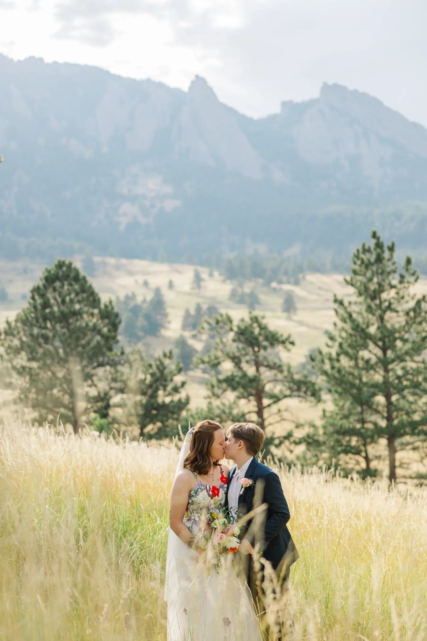 Sydney and Hannah Rusow share a kiss in a golden meadow with the Flatirons of Boulder, CO, as a backdrop.