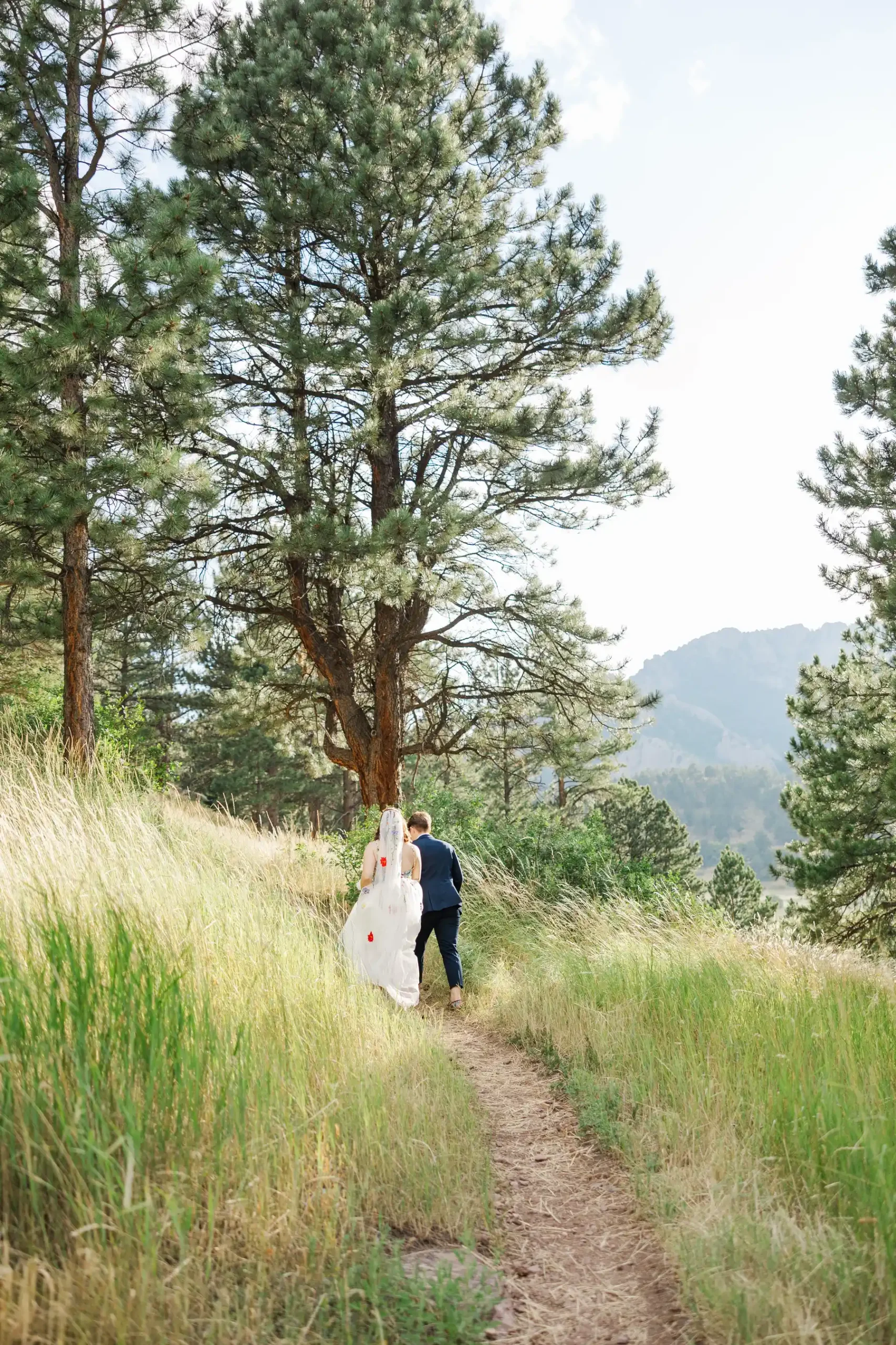Sydney and Hannah Rusow walk a mountain trail at Halfway House in Boulder, CO, in wedding attire.