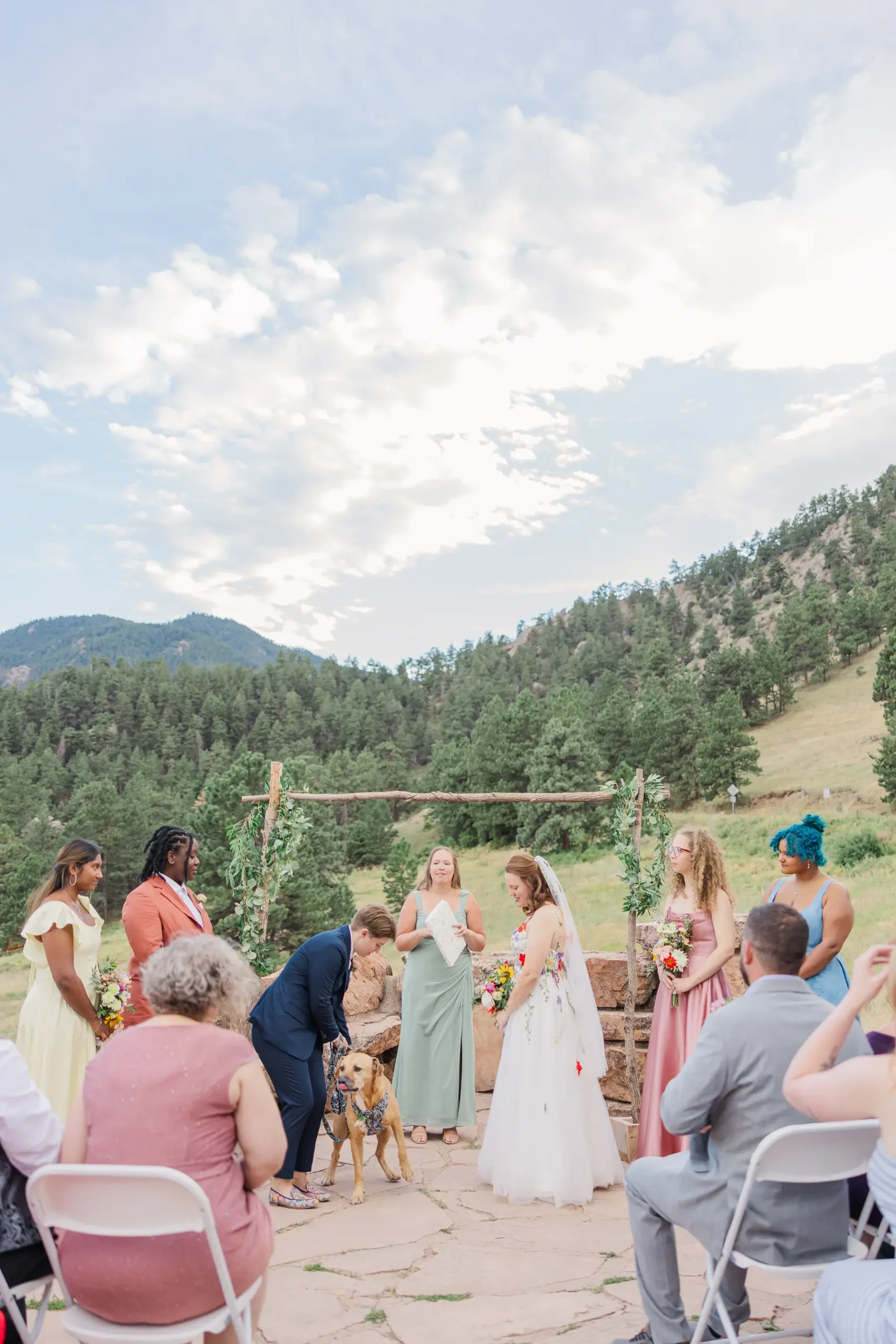 Sydney and Hannah Rusow exchange vows outdoors at Halfway House in Boulder, CO, as their dog joins the ceremony.